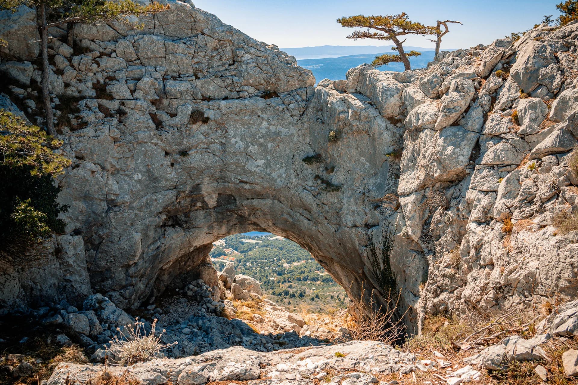 A natural opening through a limestone formation, with mountain terrain visible beyond.