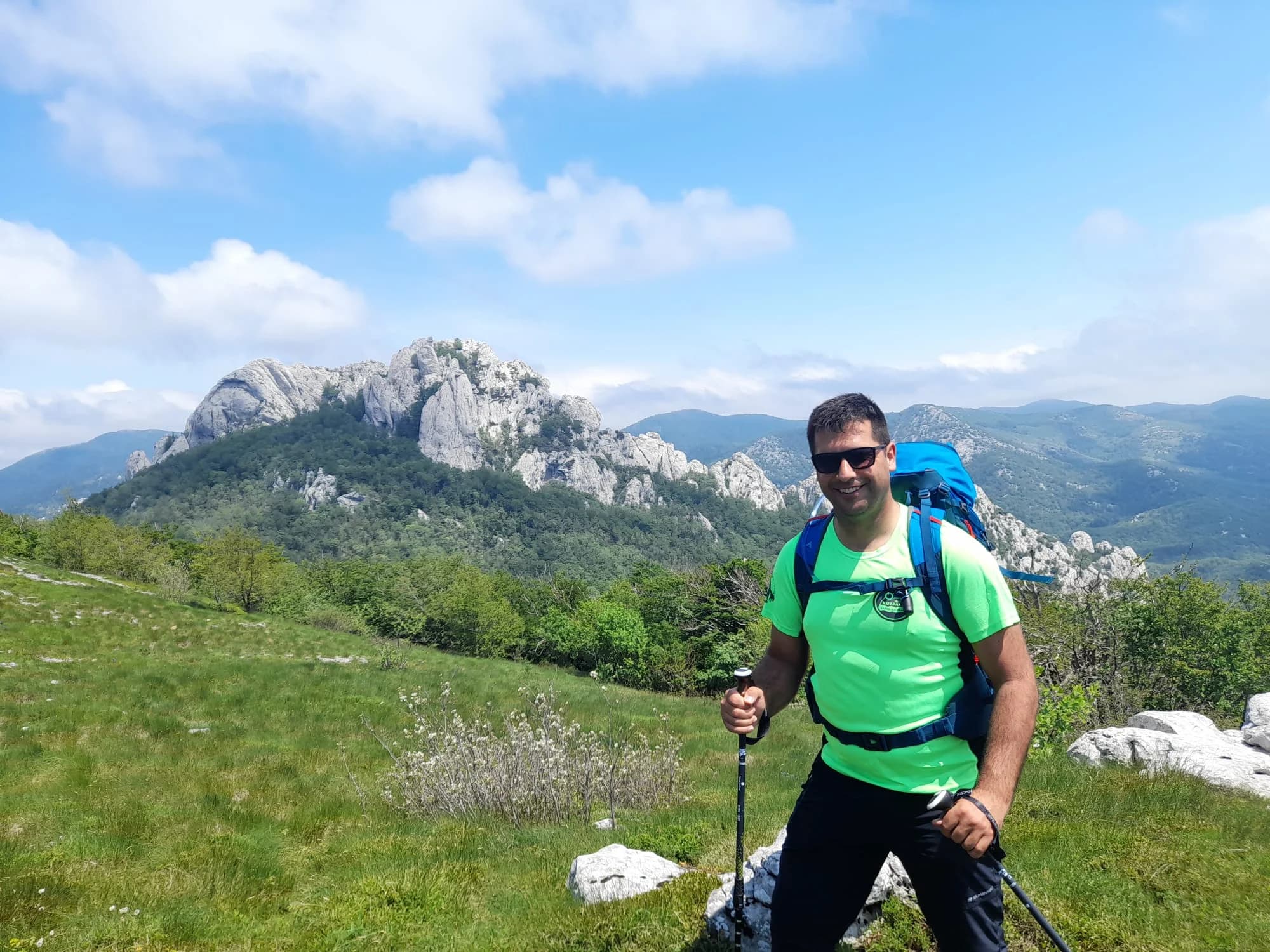 A hiker with a backpack and trekking poles in a rocky mountain landscape.
