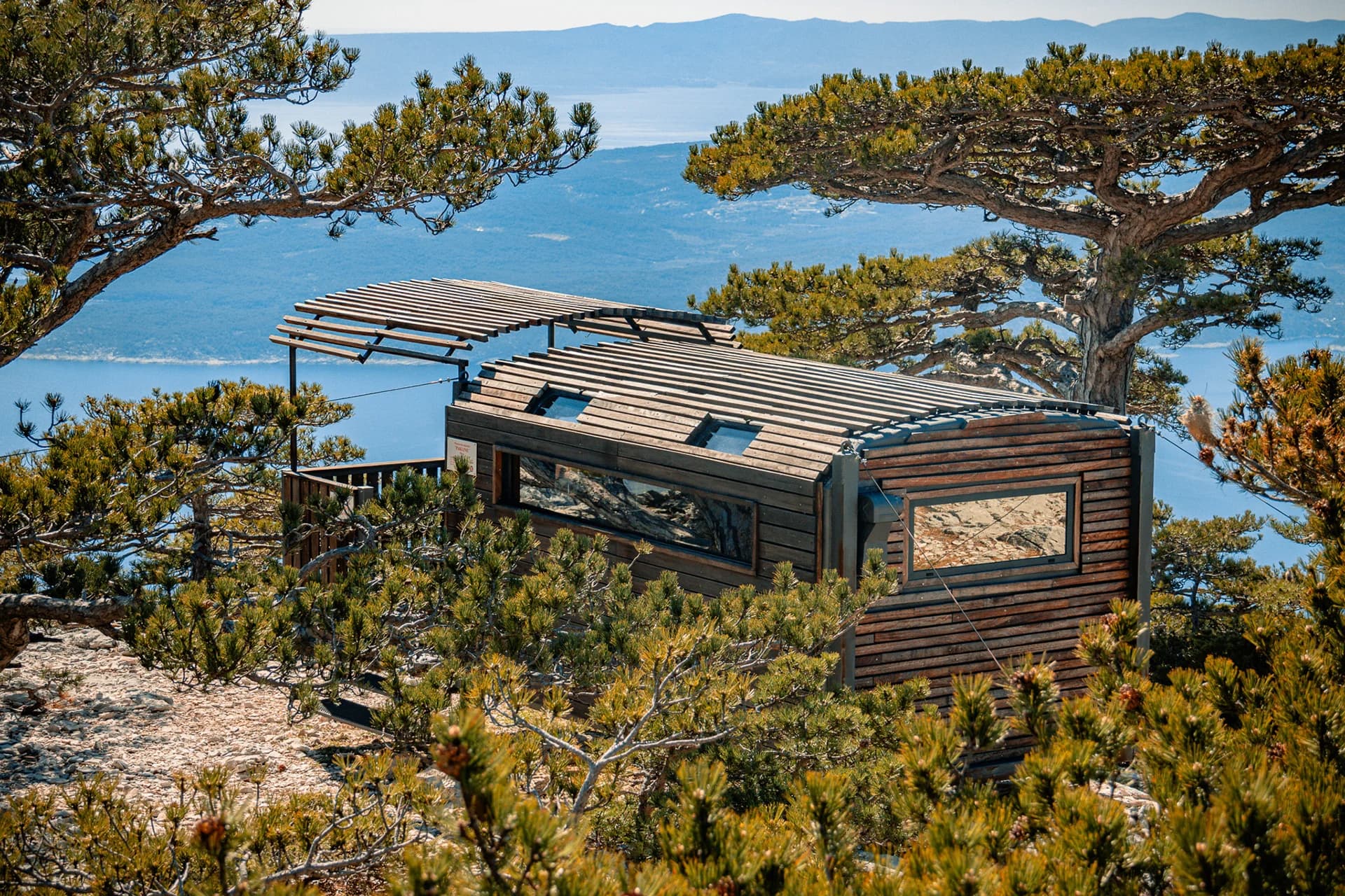 A mountain shelter among pine trees with the Adriatic in the background.