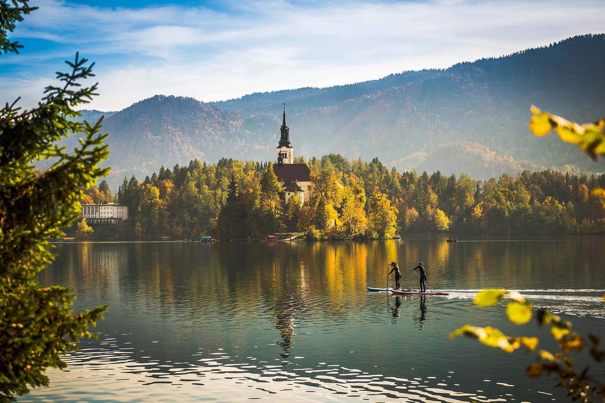 Bled's island church reflected in the lake among autumn trees and wooded hills.