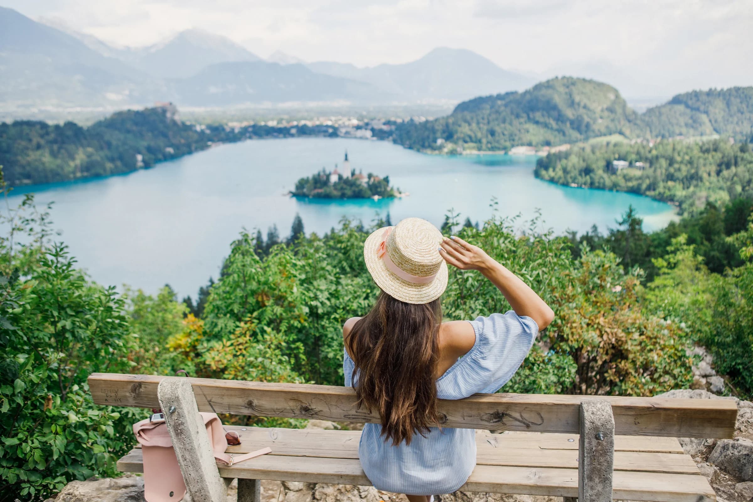 A visitor seated at a wooden lookout above Lake Bled and its island.