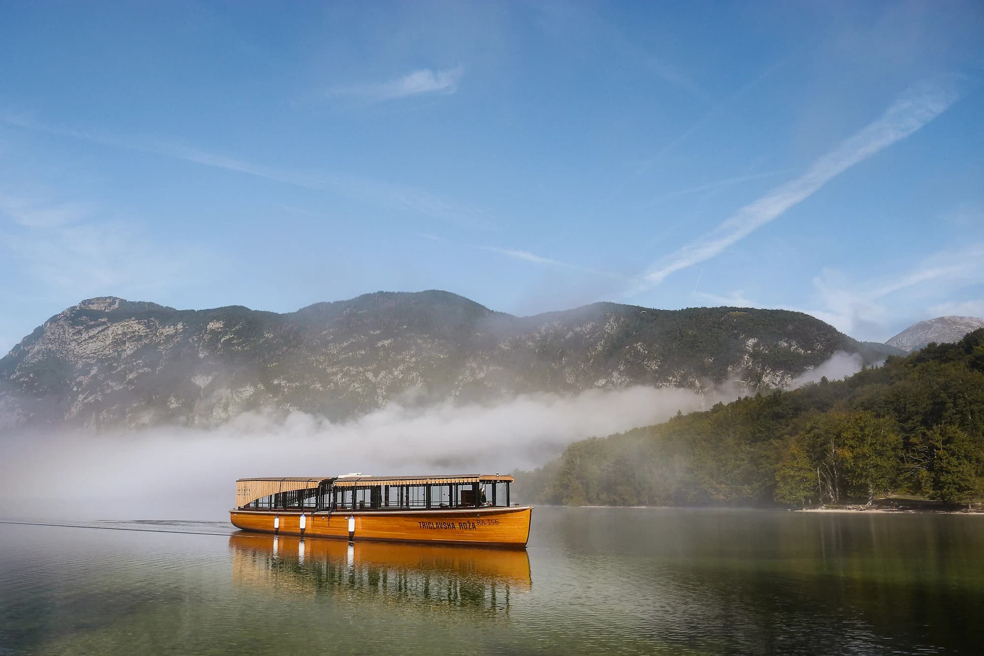 The Triglavska roža passenger boat on Lake Bohinj beneath misty mountain slopes.