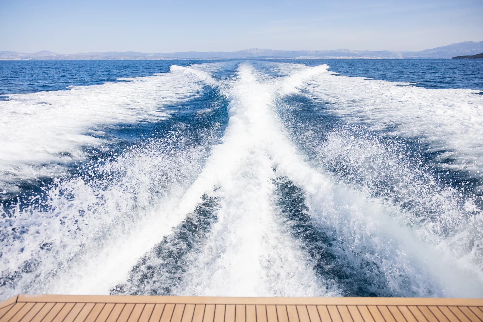 The wake behind a cruising boat, with a low coastline on the horizon.