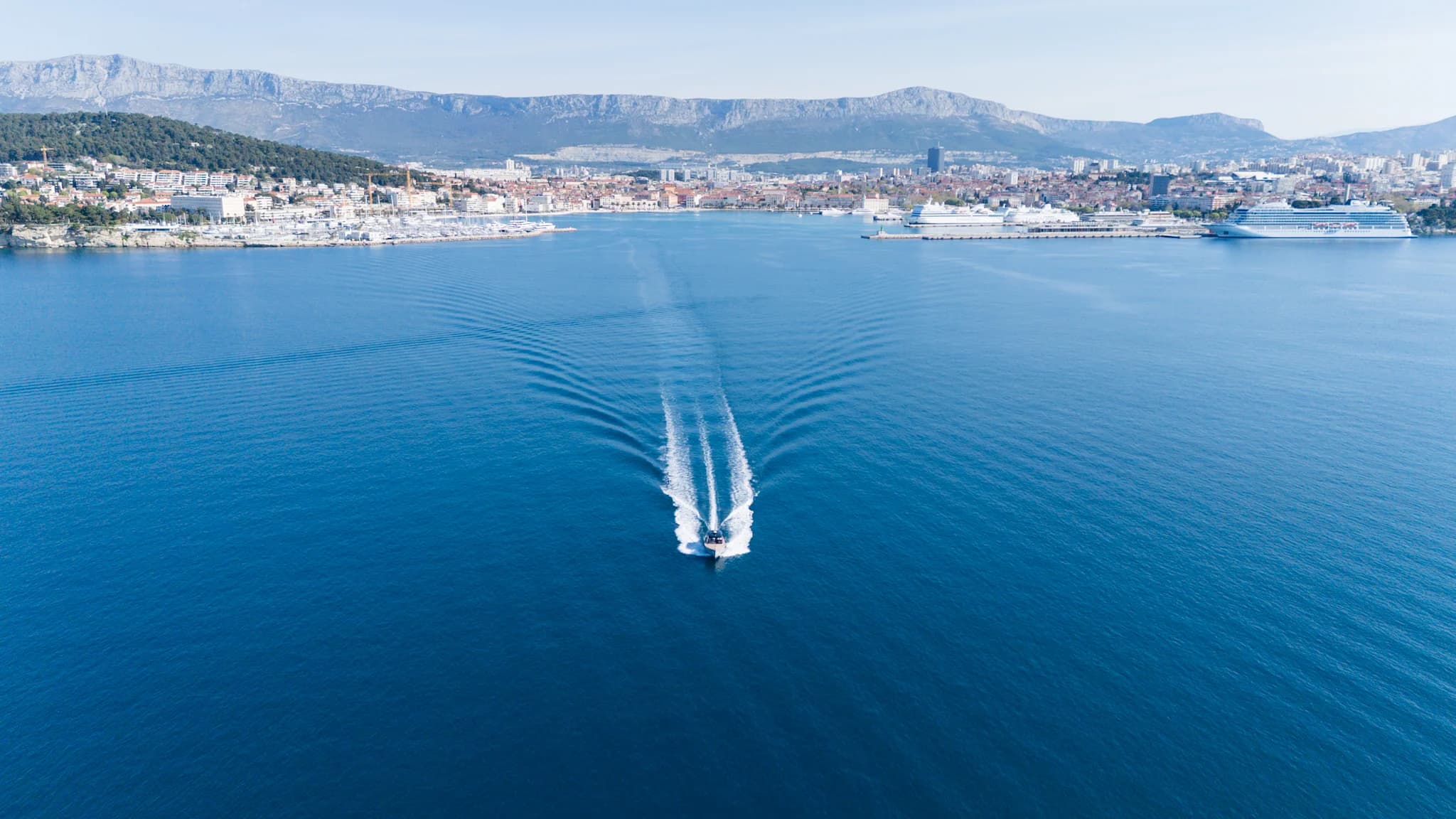 A boat leaving a broad wake in front of Split’s waterfront and surrounding hills.