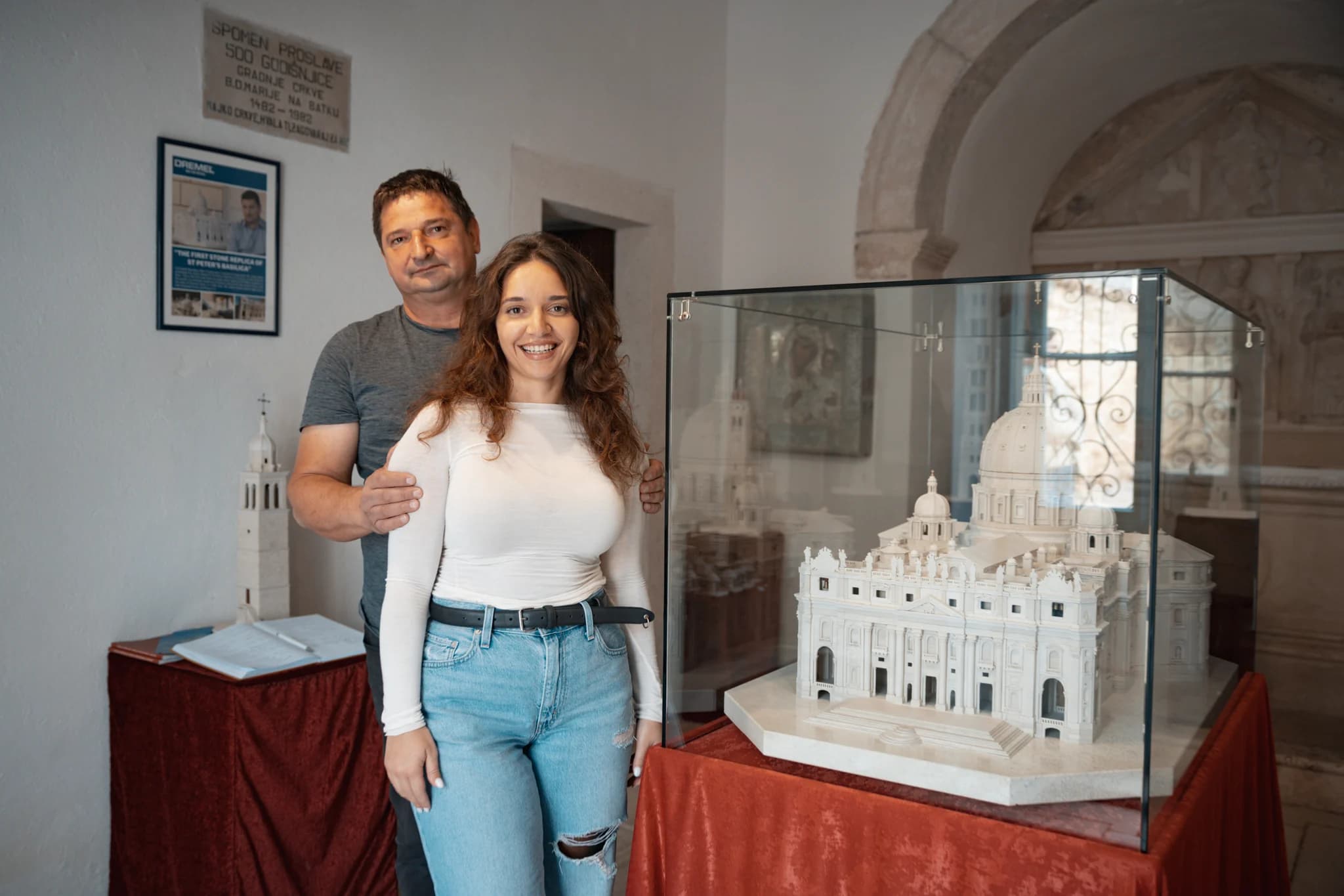 Two people beside a miniature of St. Peter’s Basilica in a glass display case.