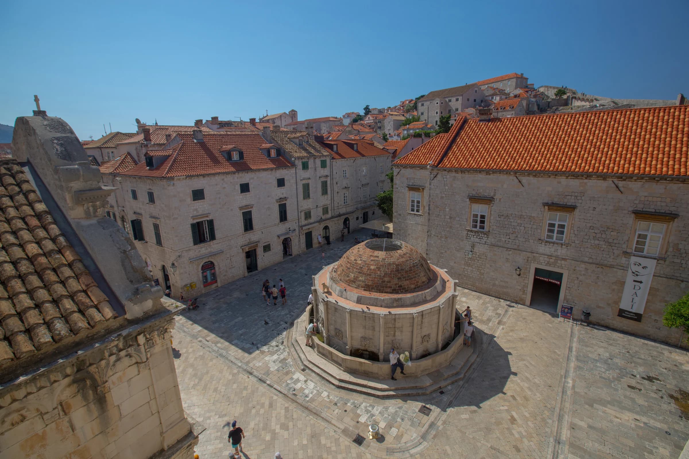 A domed stone fountain in a Dubrovnik square surrounded by old stone buildings.