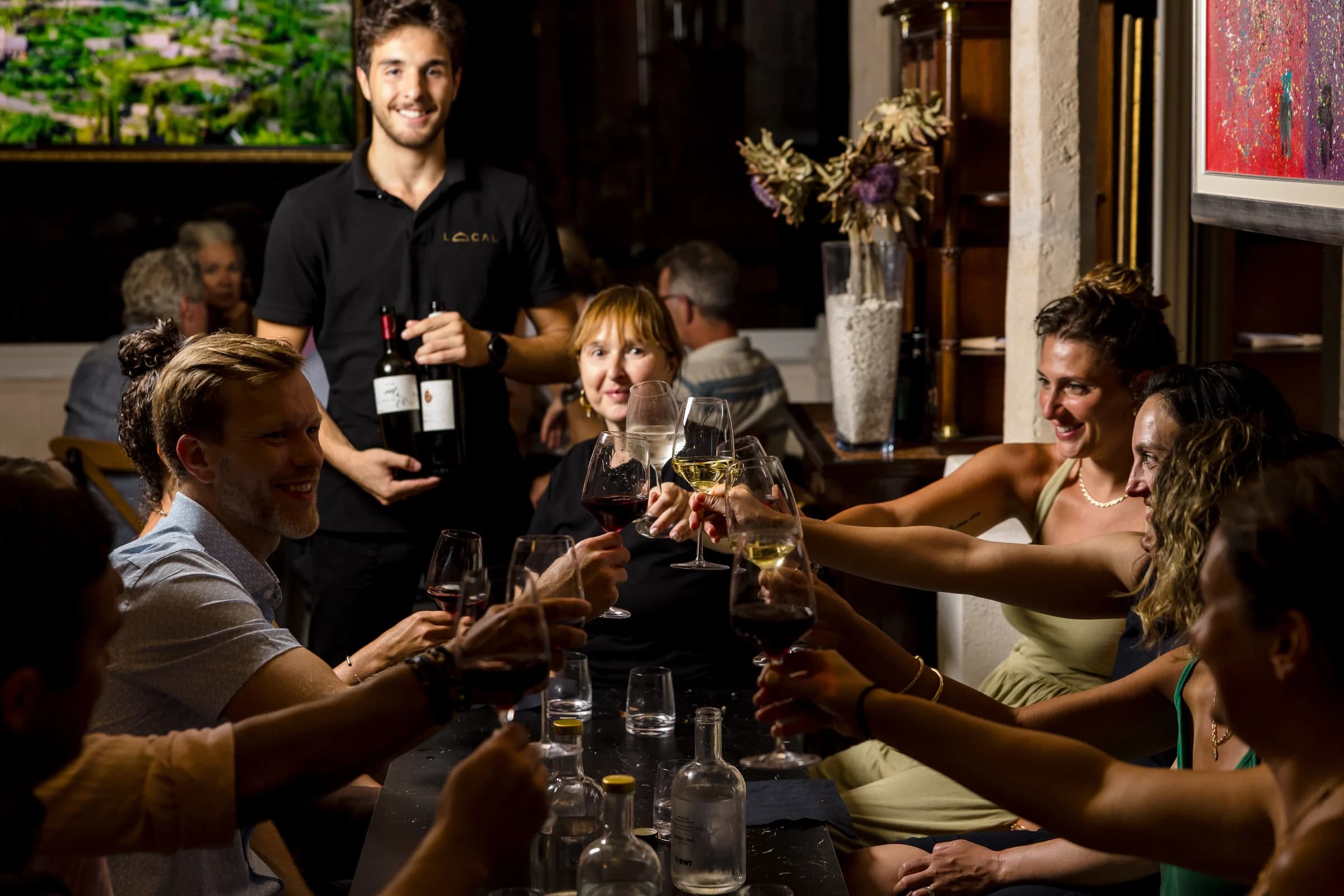 Guests raising glasses around a dining table while wine is presented.