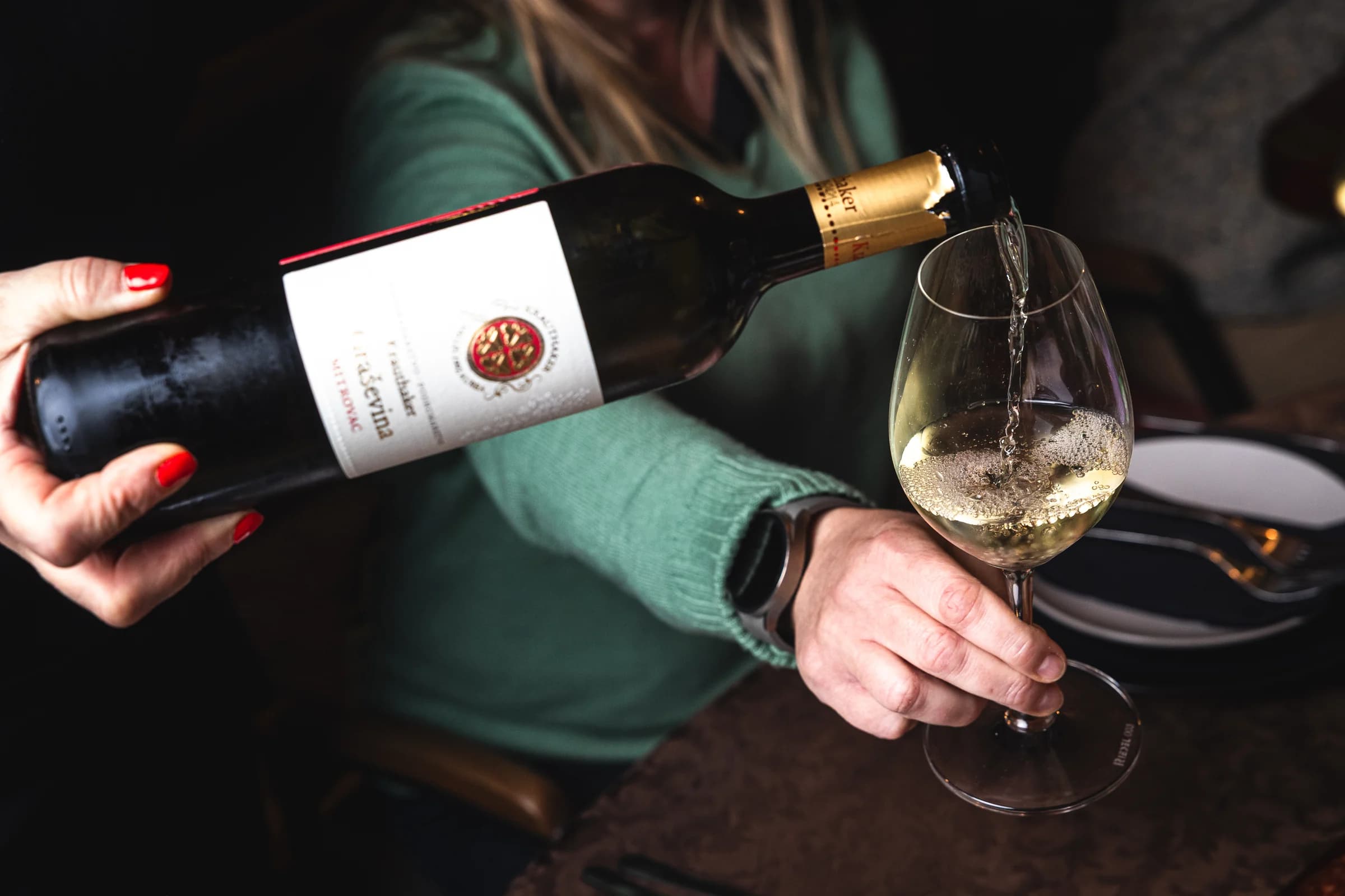 White wine being poured into a glass held beside a dining table.
