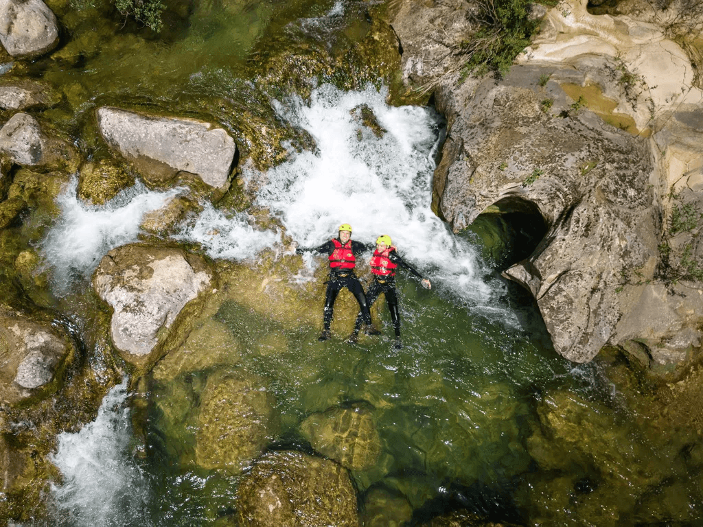 Two canyoners floating in a clear rock pool below a small cascade.