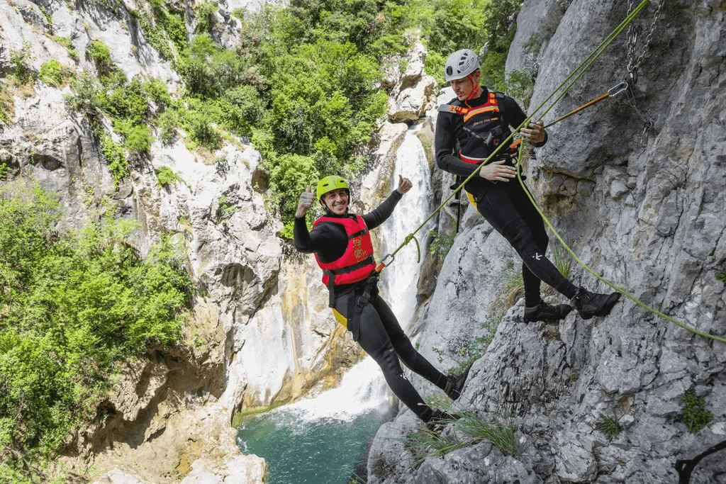Helmeted canyoners suspended on ropes beside a limestone cliff.