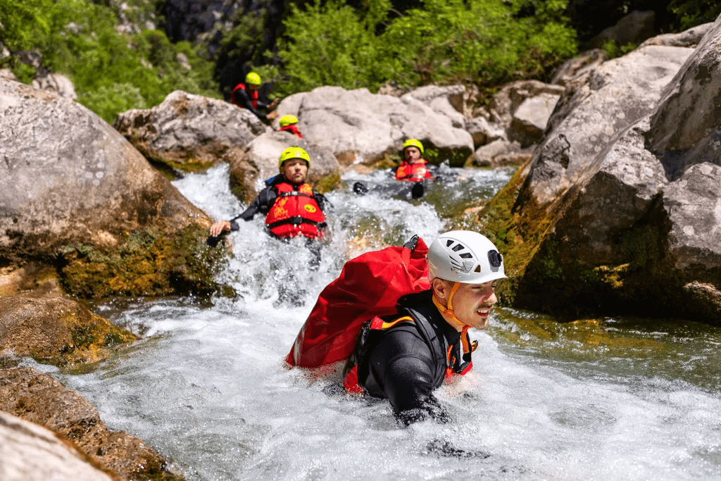 Helmeted canyoners moving through white water between river rocks.