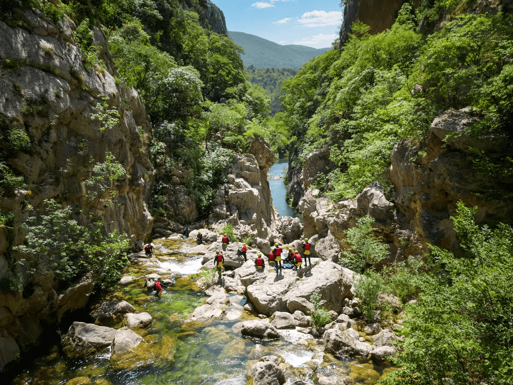 A canyoning group crossing pale rocks between the wooded walls of the Cetina canyon.