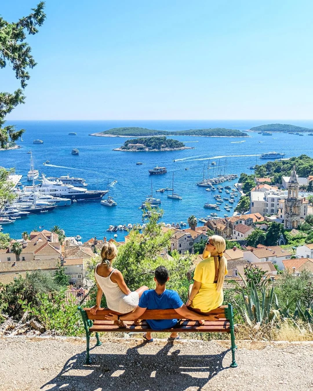 Three visitors seated on a bench overlooking Hvar’s harbour and offshore islands.