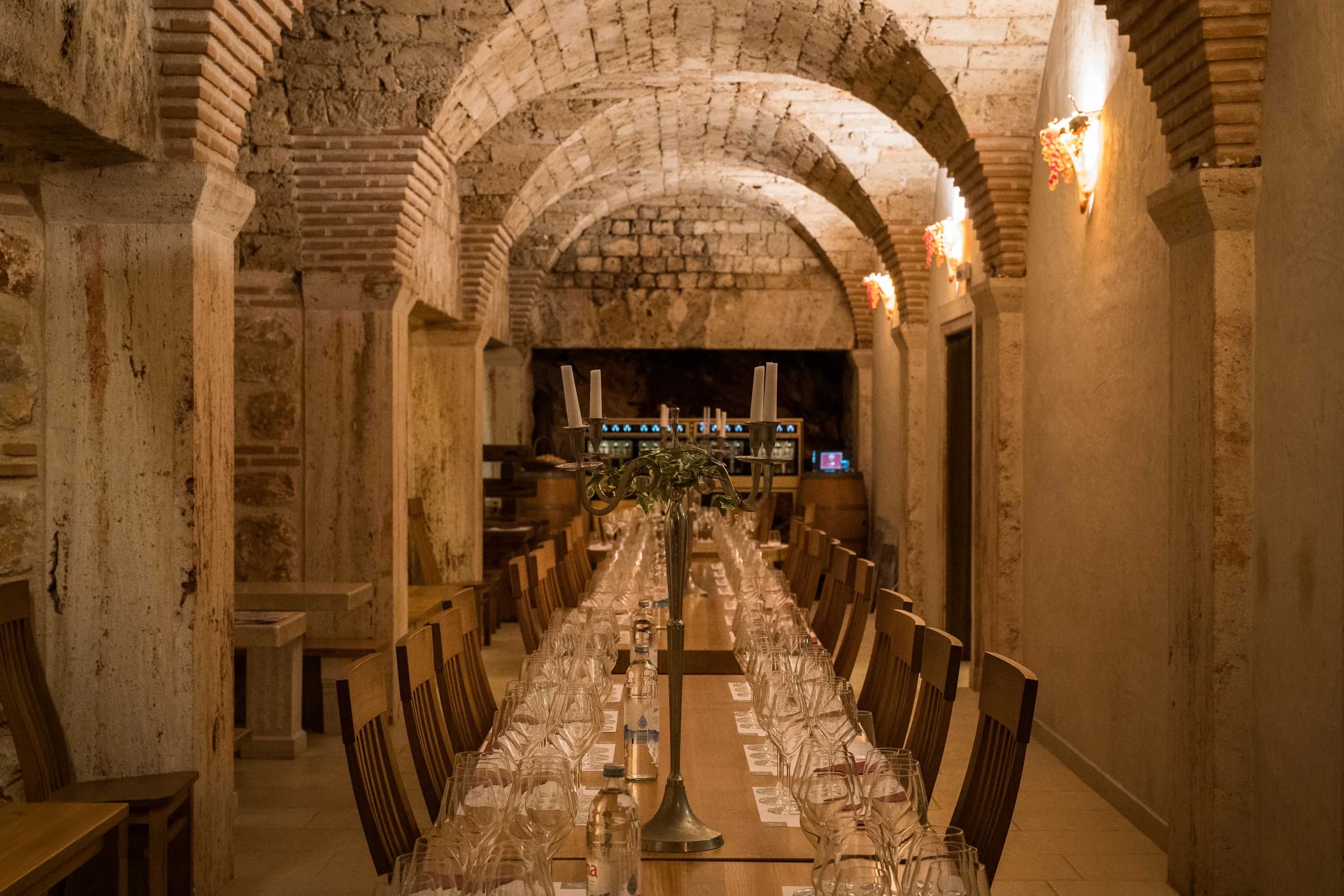 A long table set with tasting glasses inside a vaulted stone cellar.