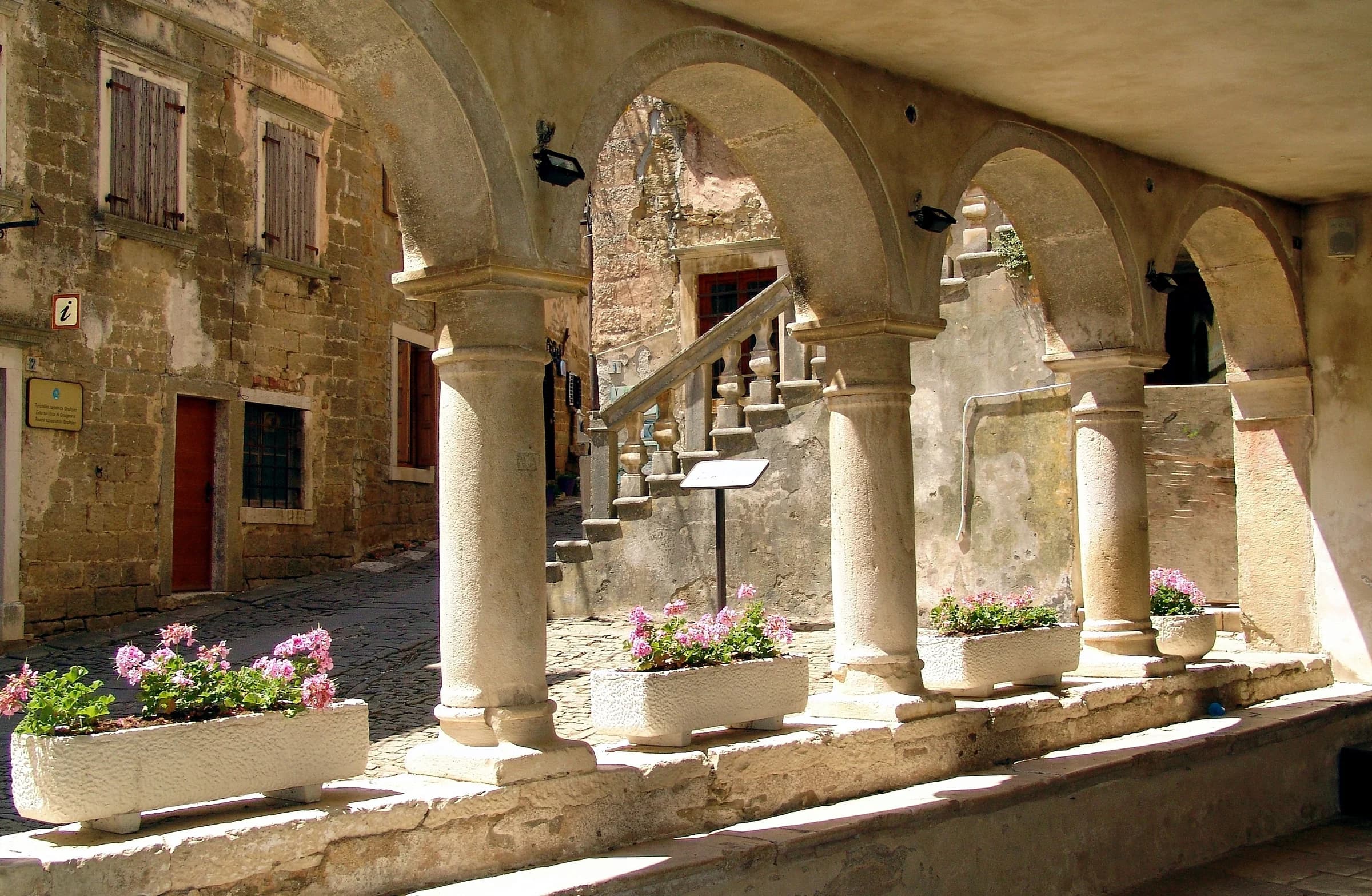 Stone columns and arches frame an old courtyard with steps and flower boxes.