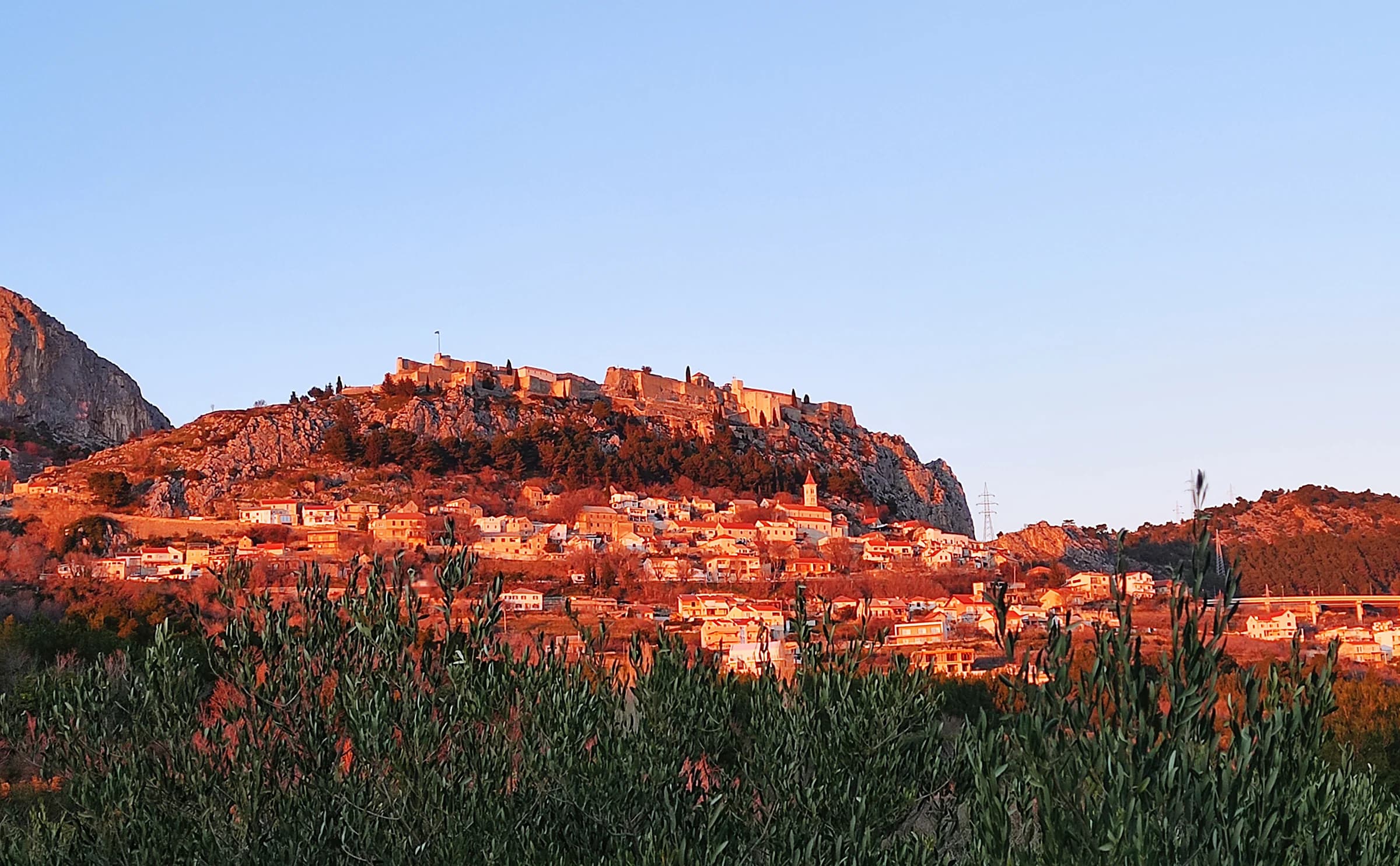 Klis Fortress and the hillside settlement below it in warm evening light.
