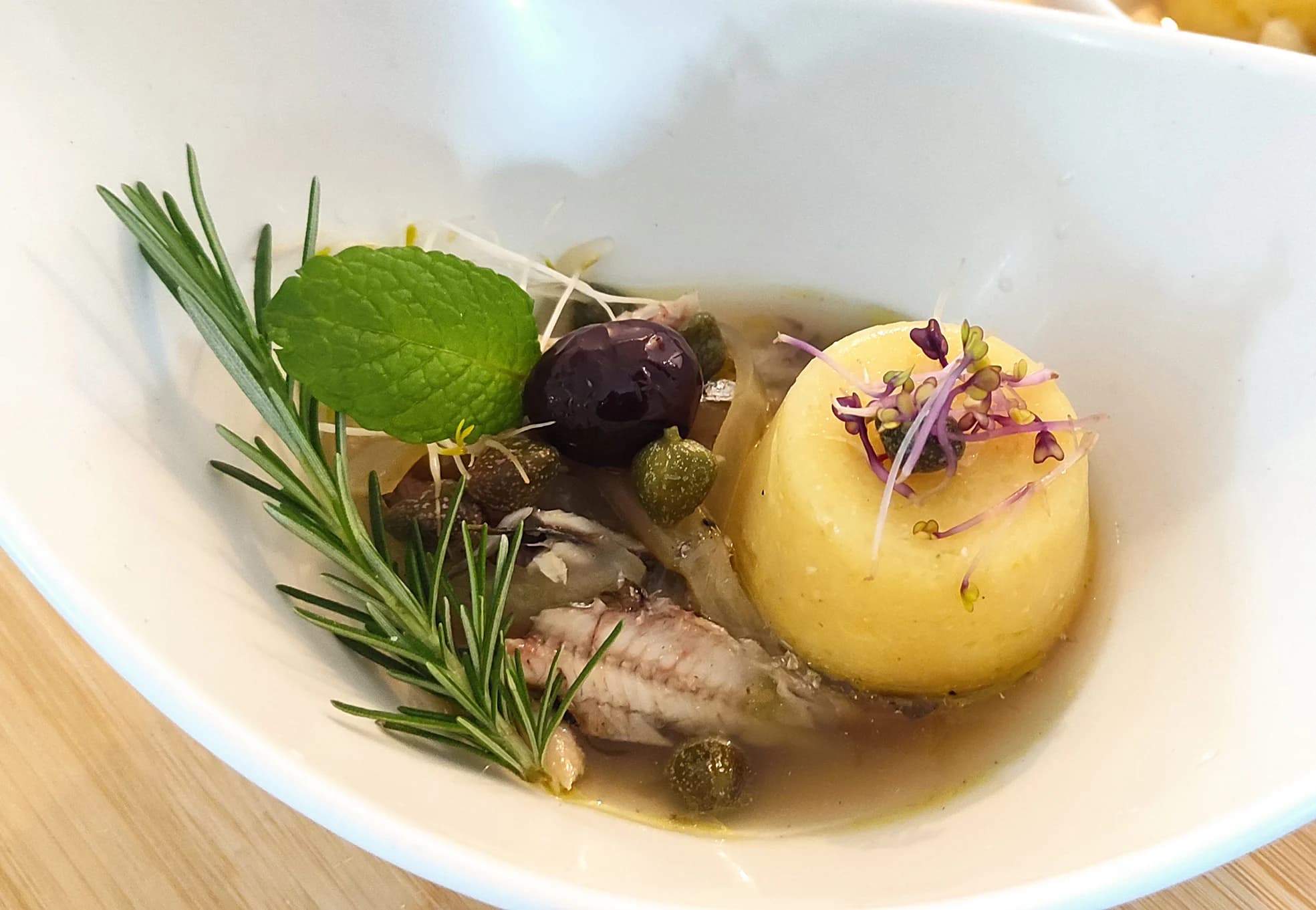 A prepared dish in a white bowl, finished with rosemary and small flowers.