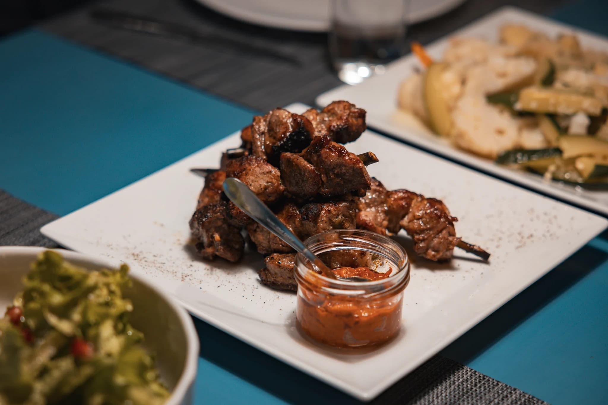 A close view of roasted meat skewers and red relish on a white plate.