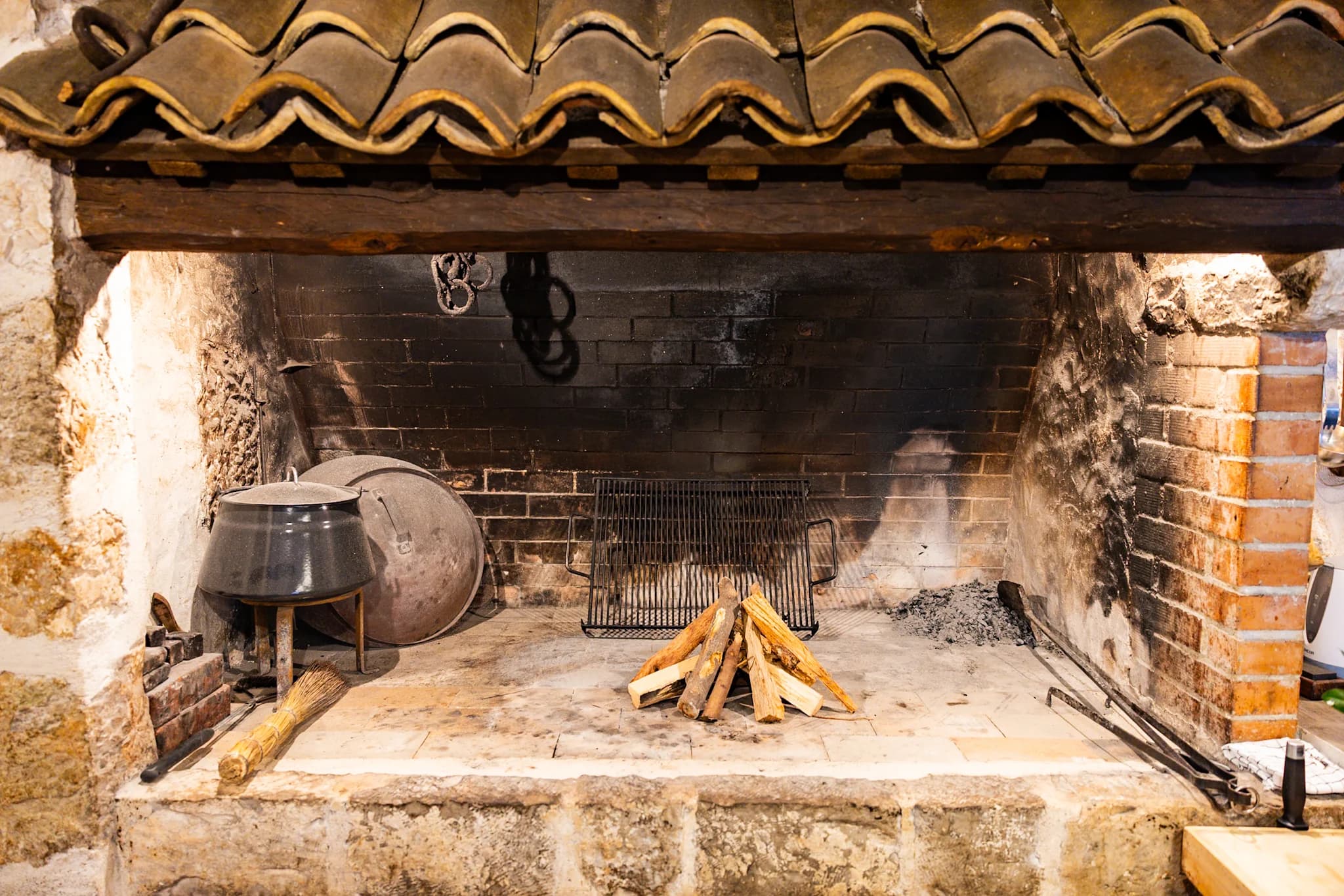 Wood laid in a broad stone hearth beneath a tiled hood, with traditional cooking pots beside it.
