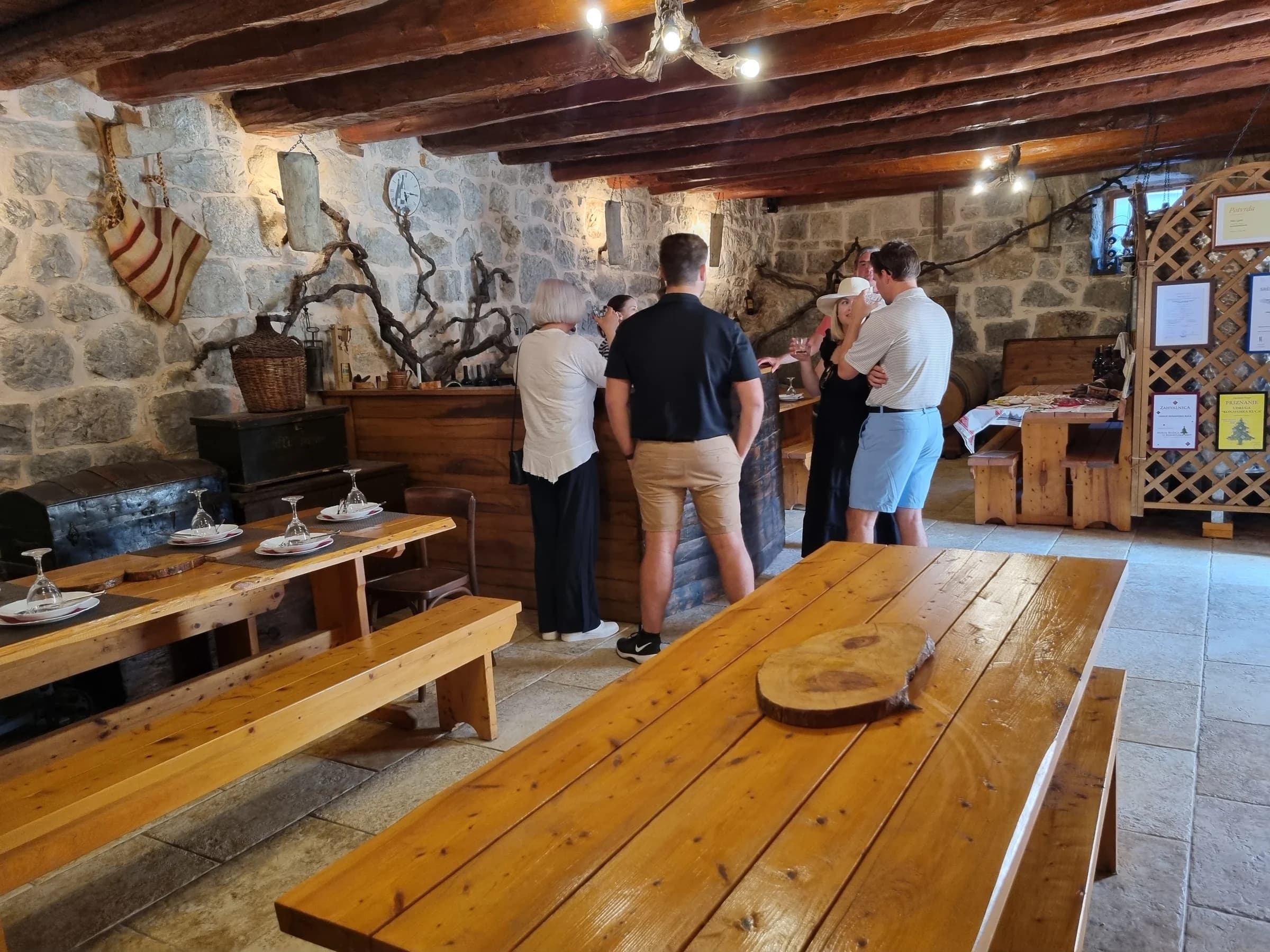 Wooden tables and a group gathered at a counter in a stone cellar.