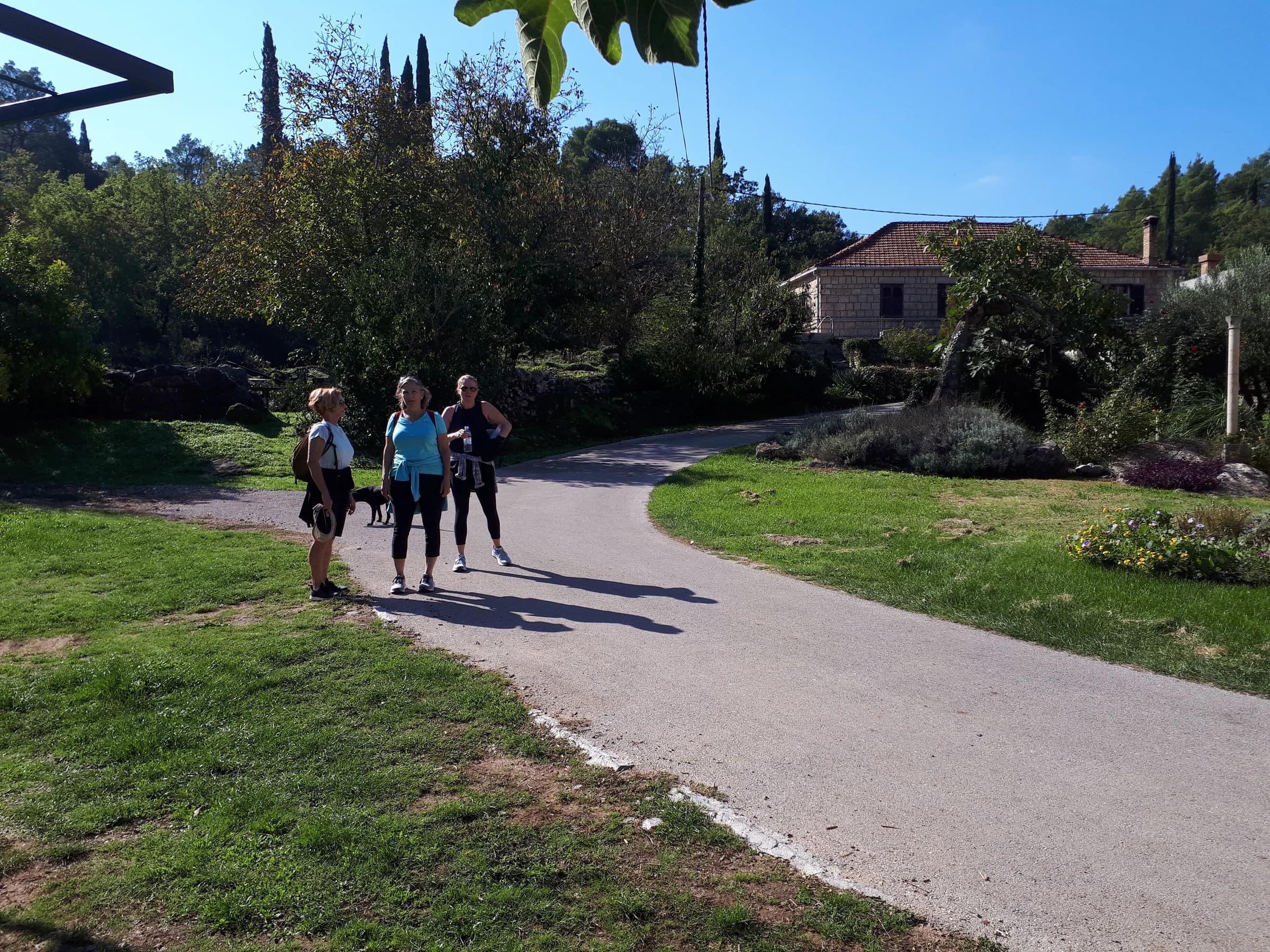 Walkers on a quiet paved lane between village gardens and stone buildings.