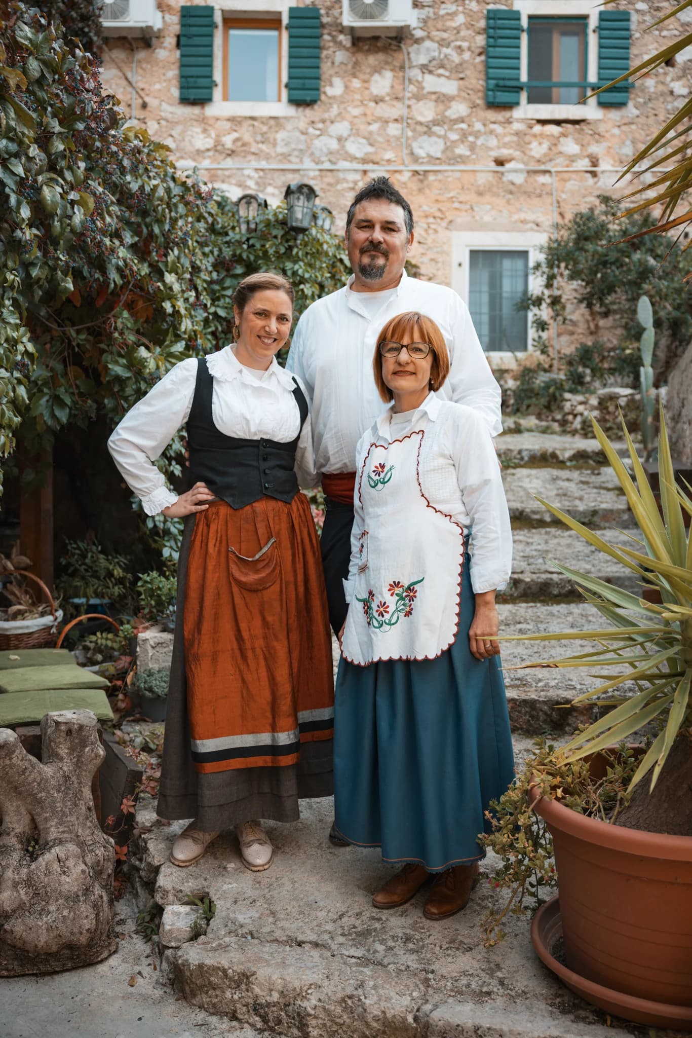 Three people standing on stone steps outside a stone house.