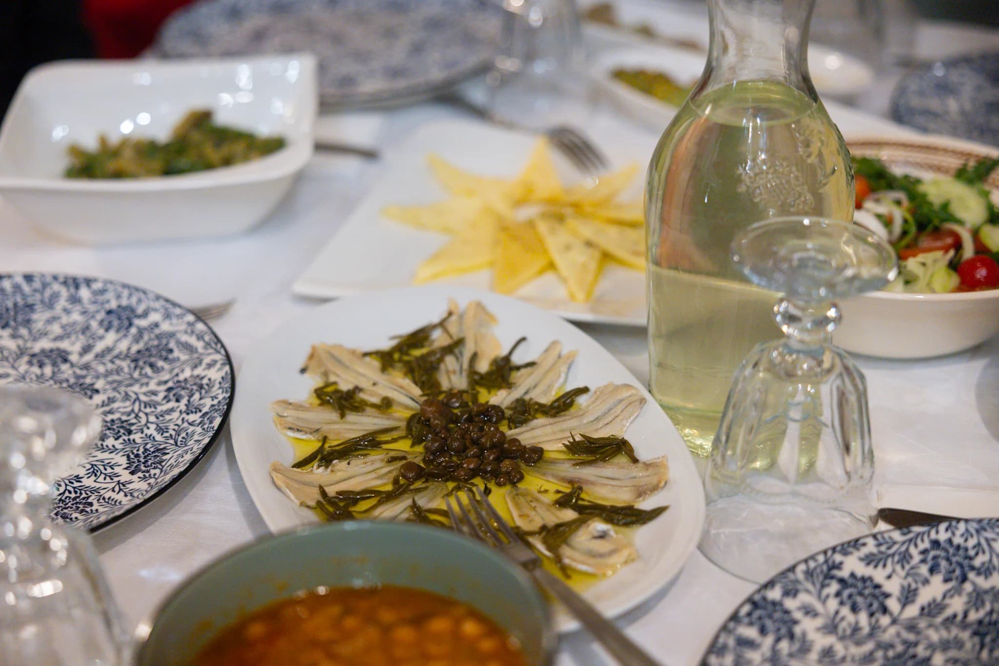 Plates of food, a glass bottle and drinking glasses on a white tablecloth.