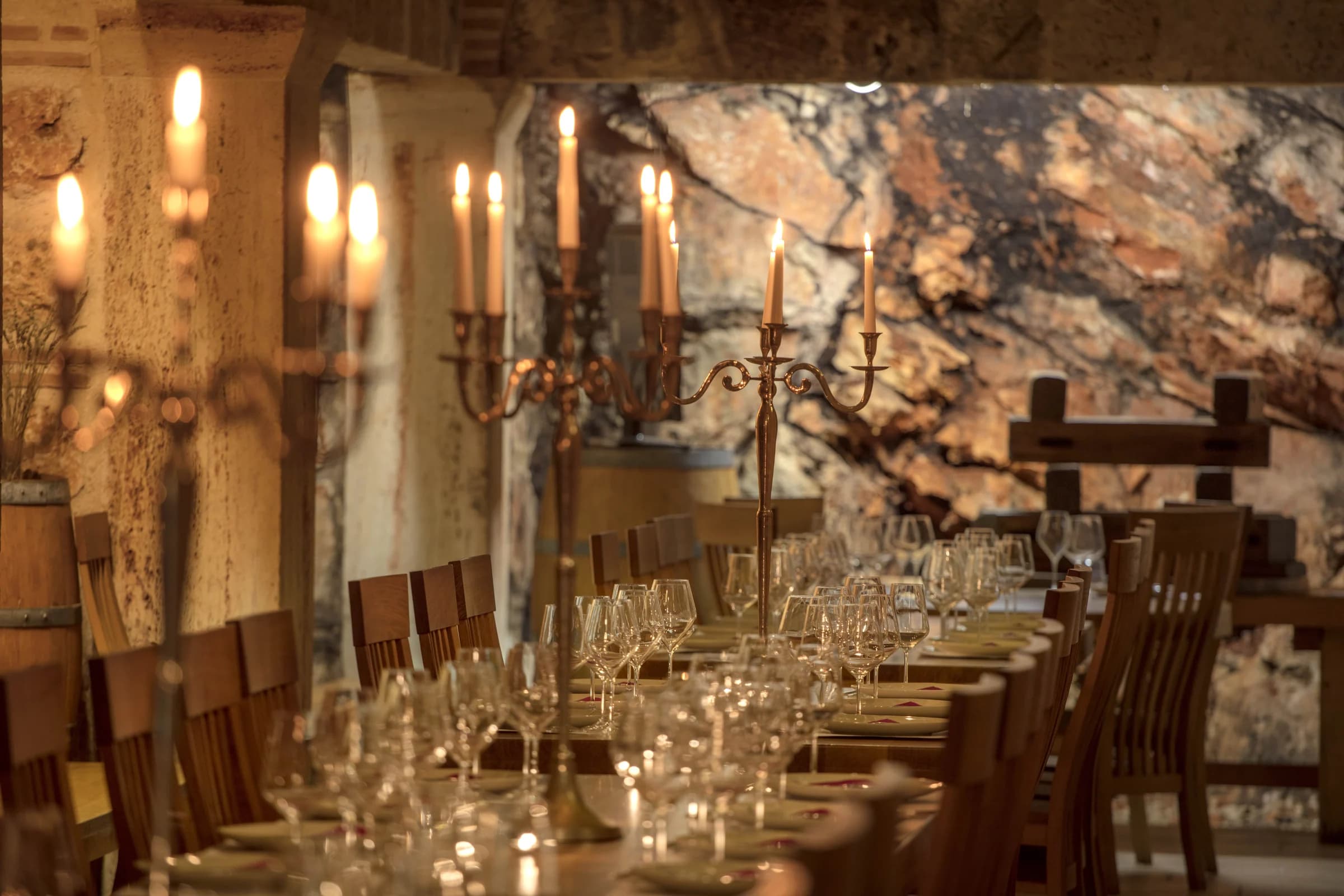 Wine glasses and candles line a long tasting table inside a stone cellar.