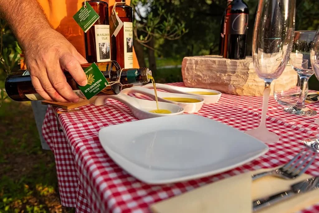 Olive oil being poured into tasting dishes on a checked tablecloth.