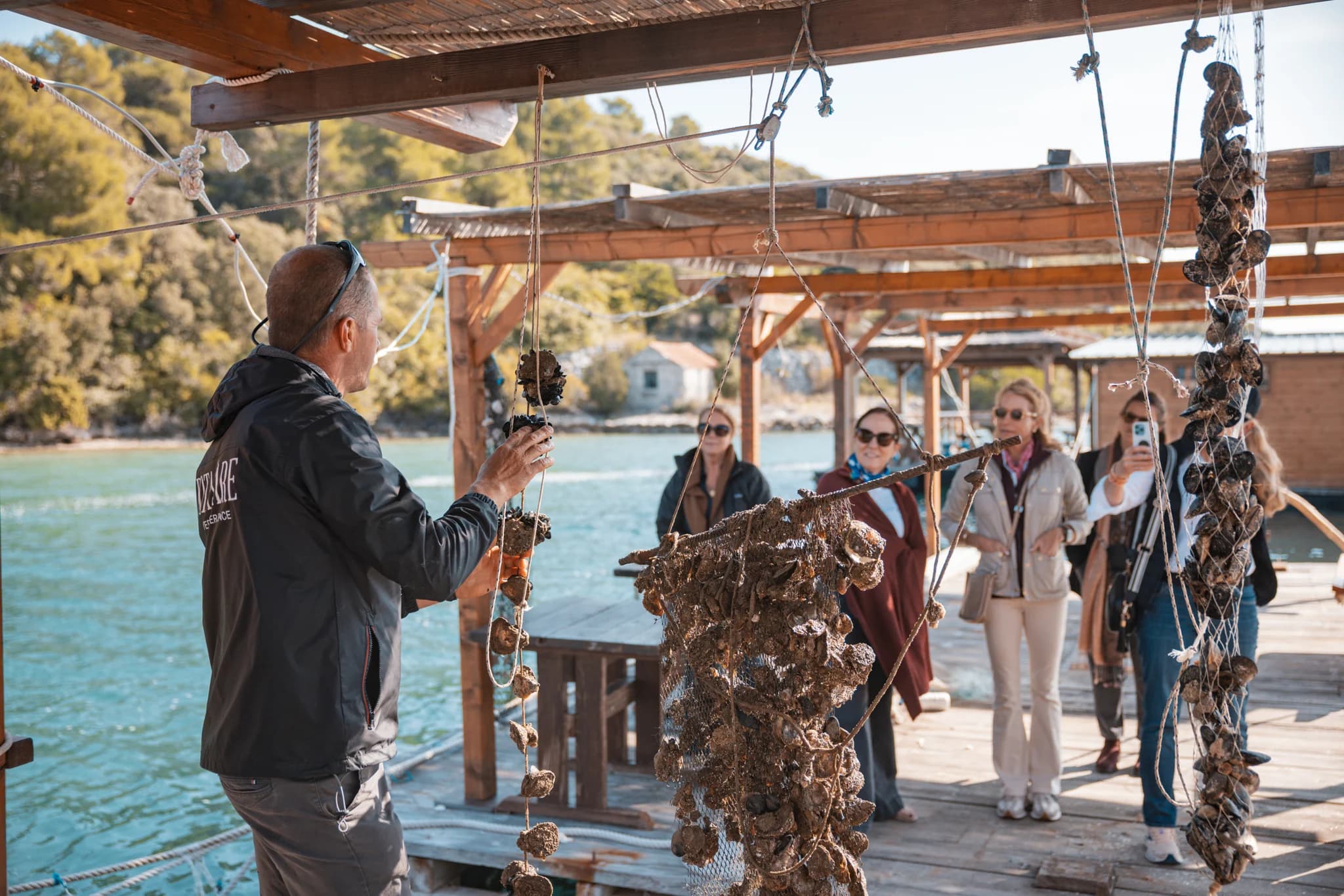 A man showing oyster clusters to visitors on a wooden dock over the water.
