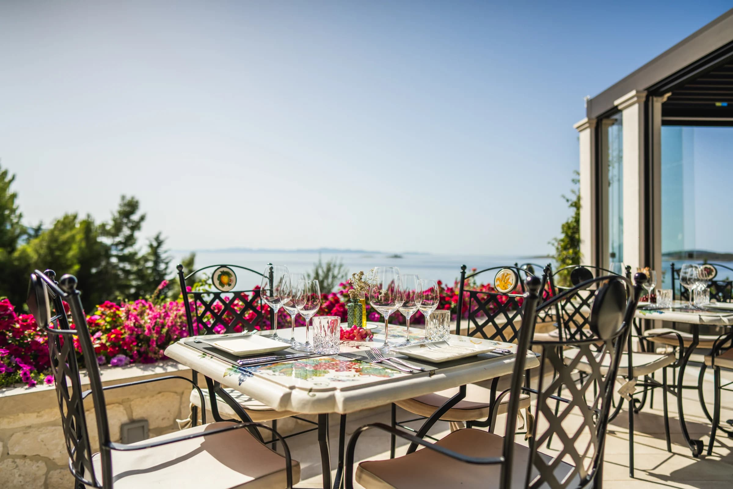 A table set with wine glasses on a terrace overlooking the sea.