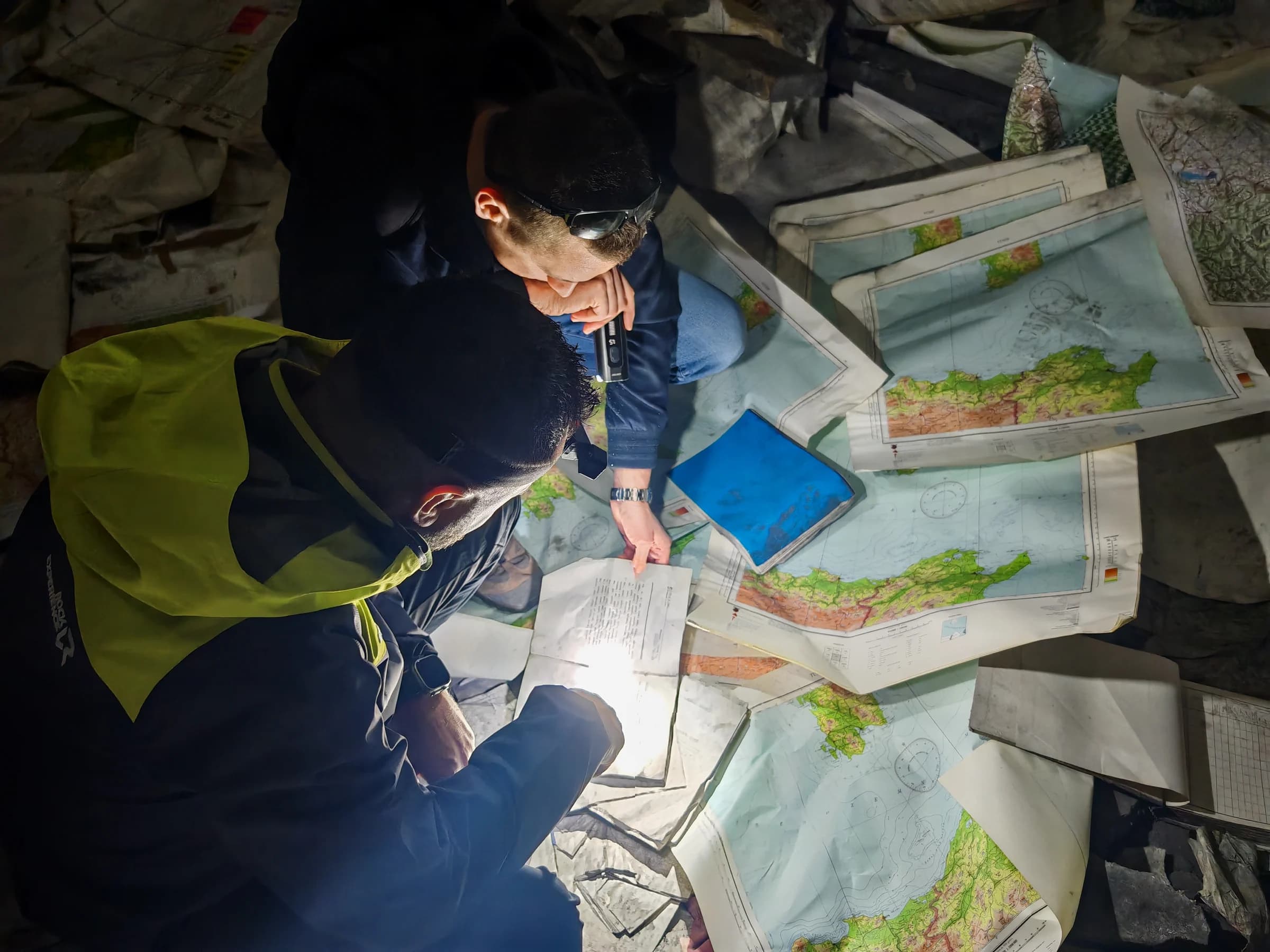 Visitors examine scattered maps and documents by torchlight.