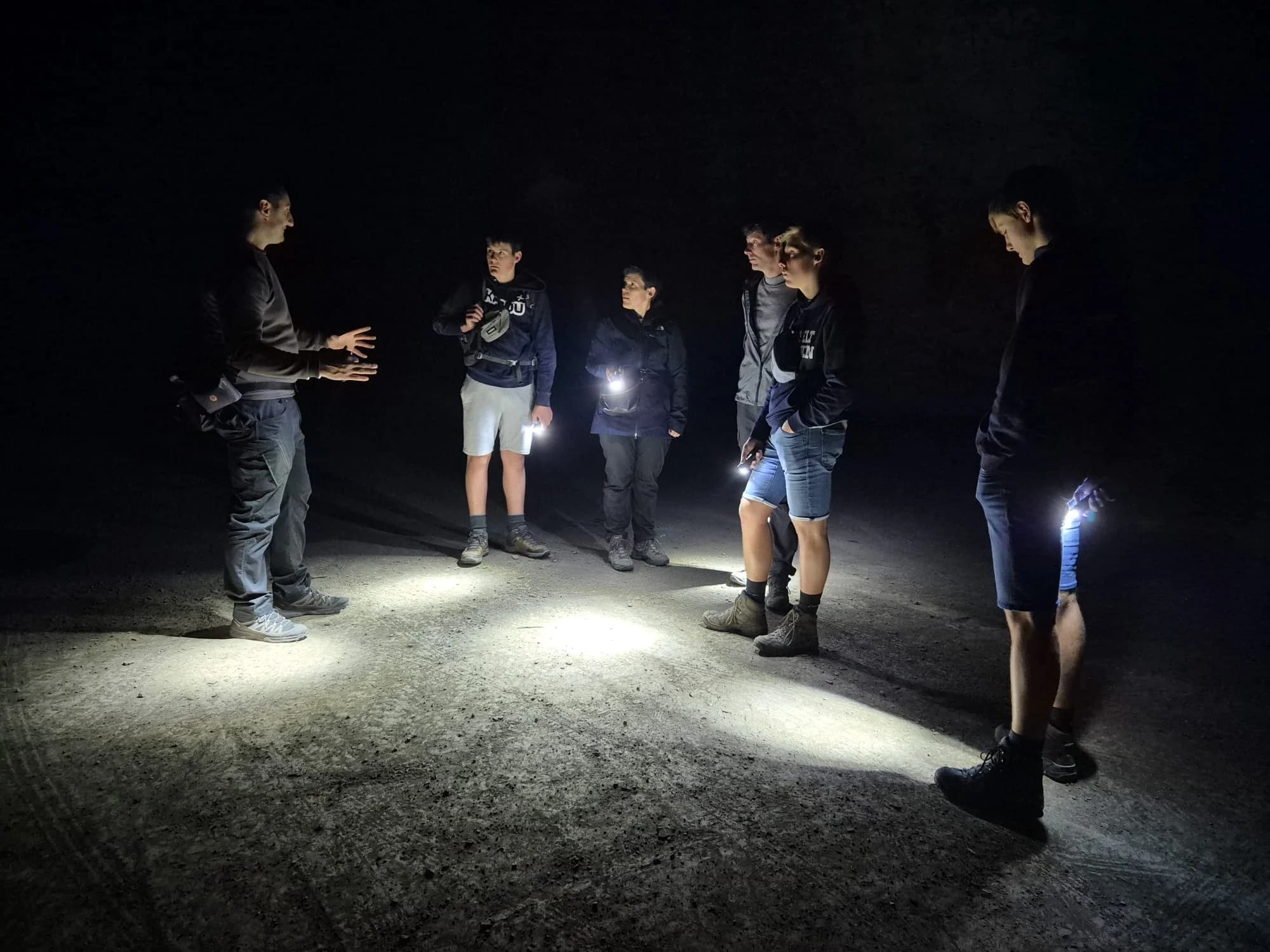 A small group stands inside a dark tunnel illuminated by handheld torches.