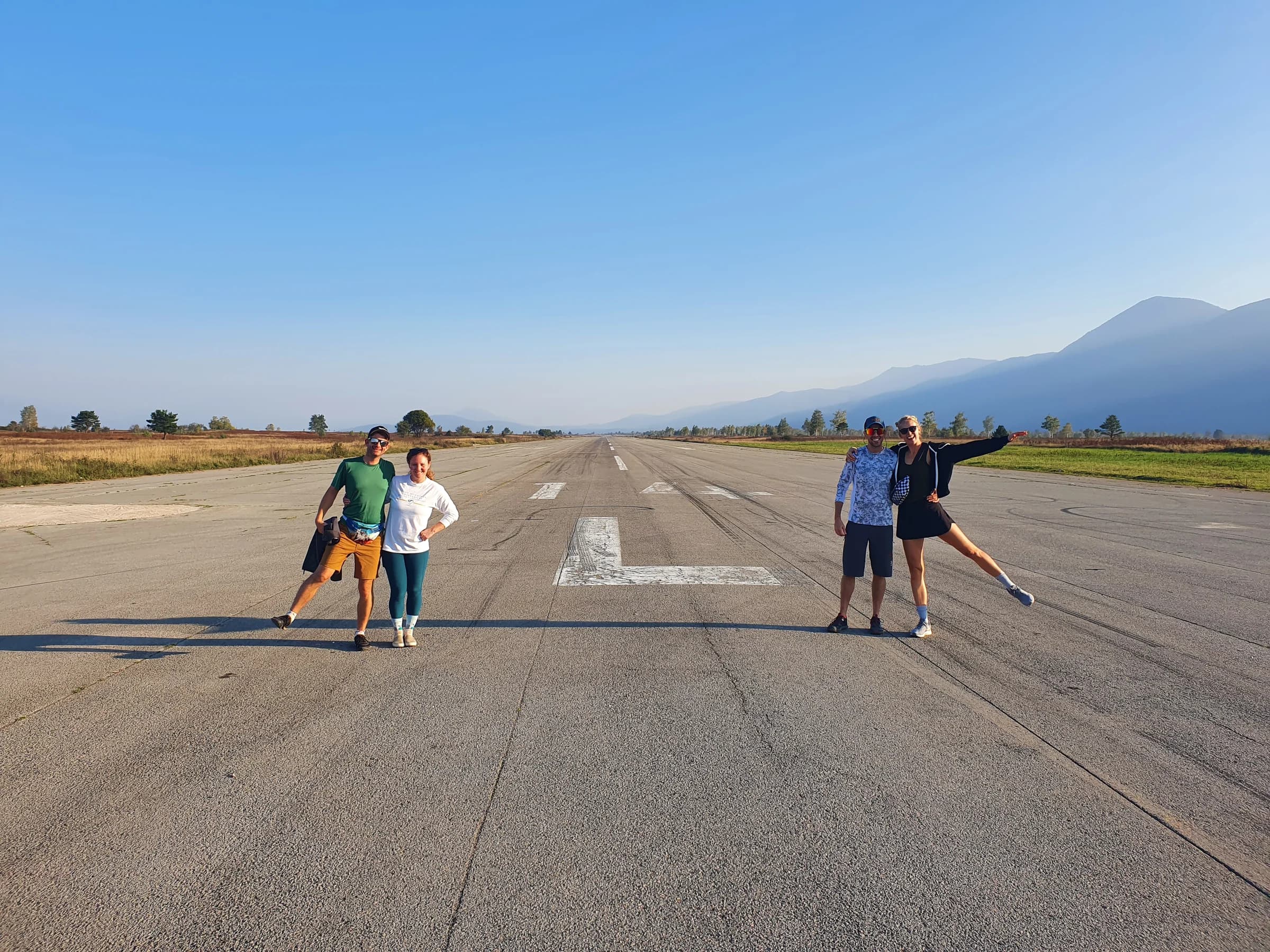 Four visitors stand on a long runway with low mountains in the distance.