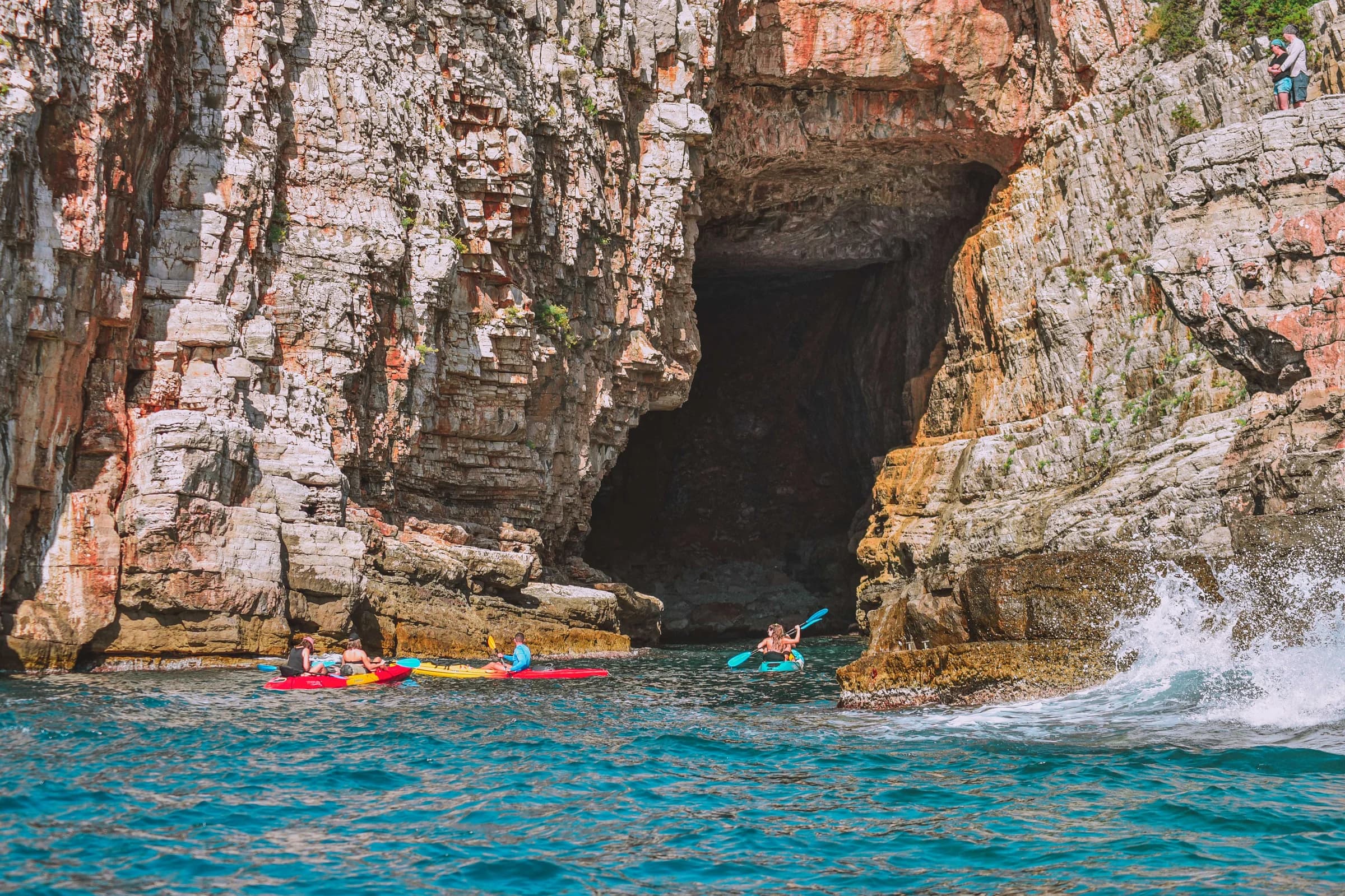 Kayakers beside a tall cave opening in the rocky coastline.