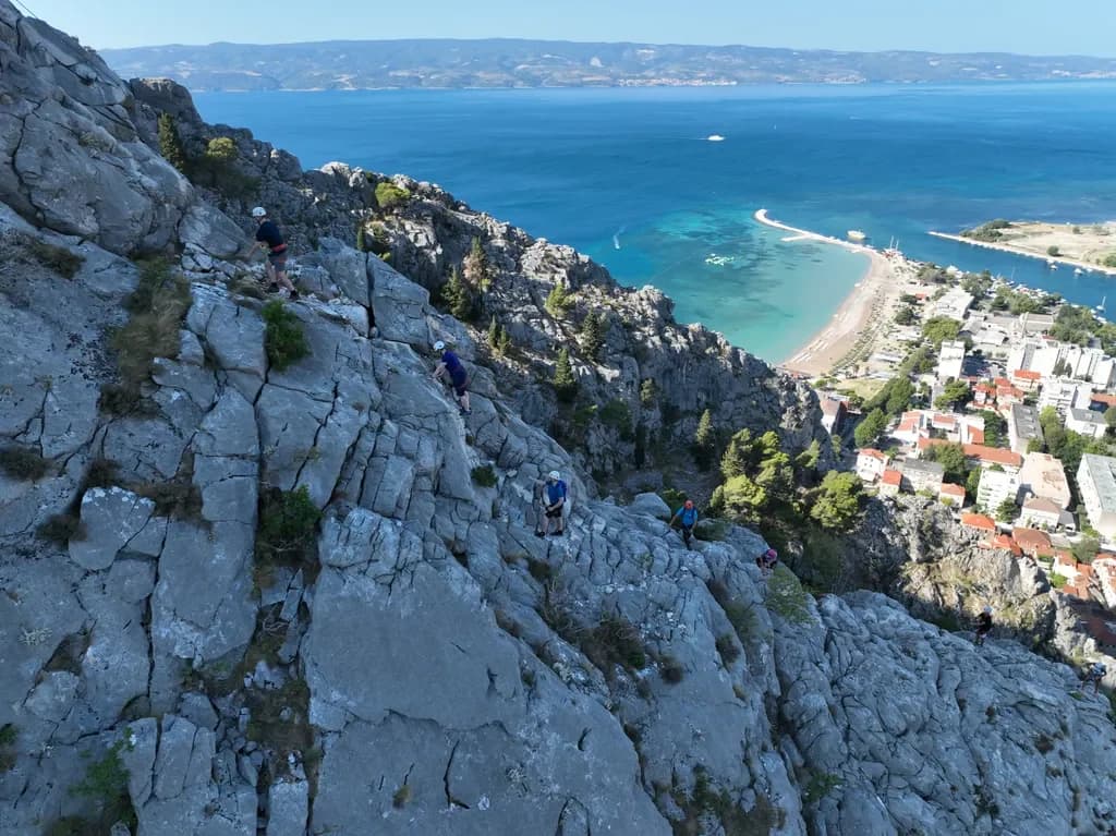 Climbers following a line across pale limestone above the coast.