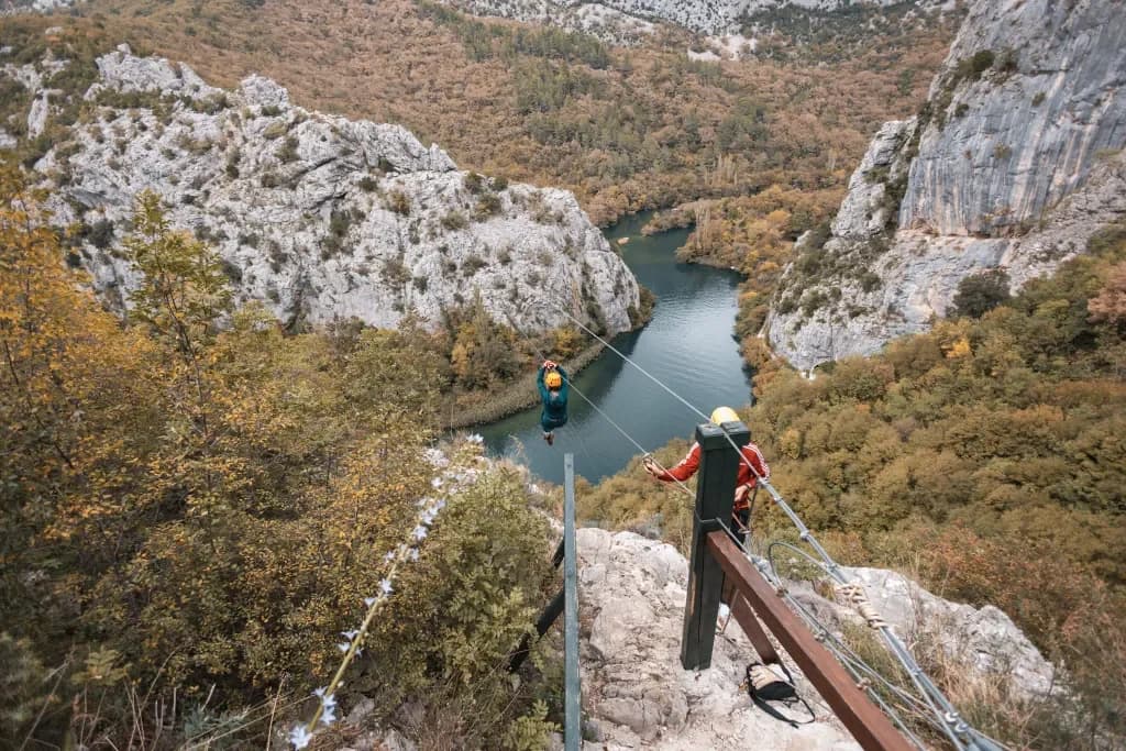 Helmeted participants at a zipline platform overlooking the river and steep canyon walls.