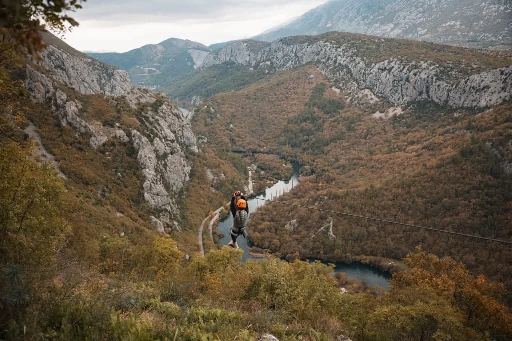 A helmeted zipline participant suspended above the Cetina River between wooded canyon slopes.