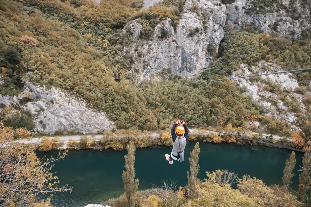 A helmeted participant suspended above the river on a zipline.