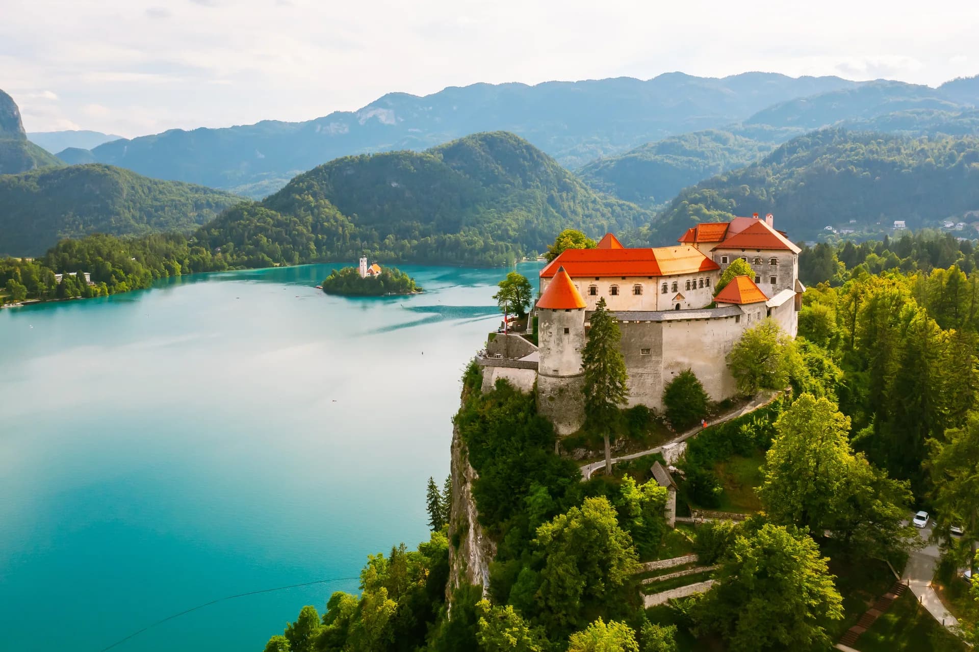 Bled Castle rises above the lake, with wooded hills and mountains beyond.
