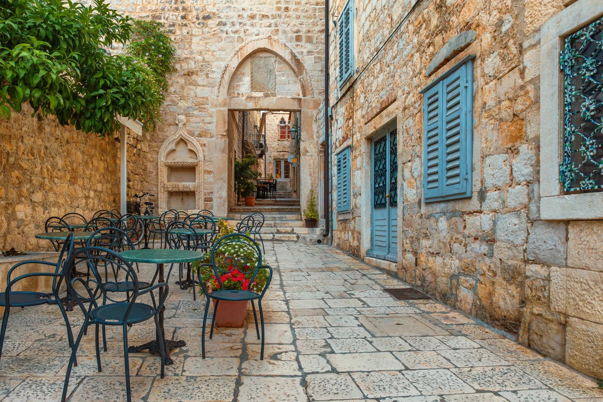 Cafe tables and blue shutters line a quiet stone lane.