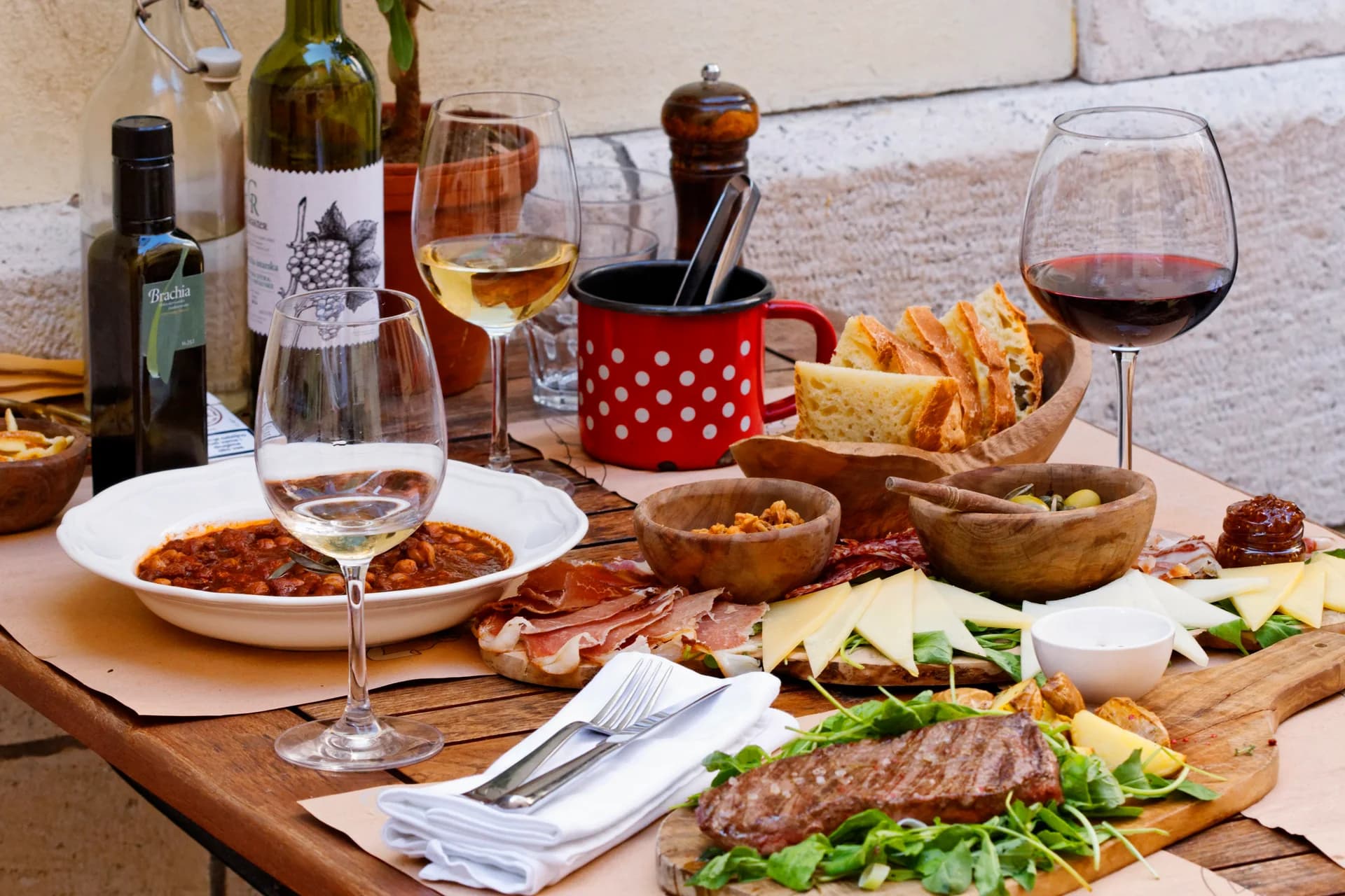 Wine, bread, cheese and cured meats arranged on a lunch table.