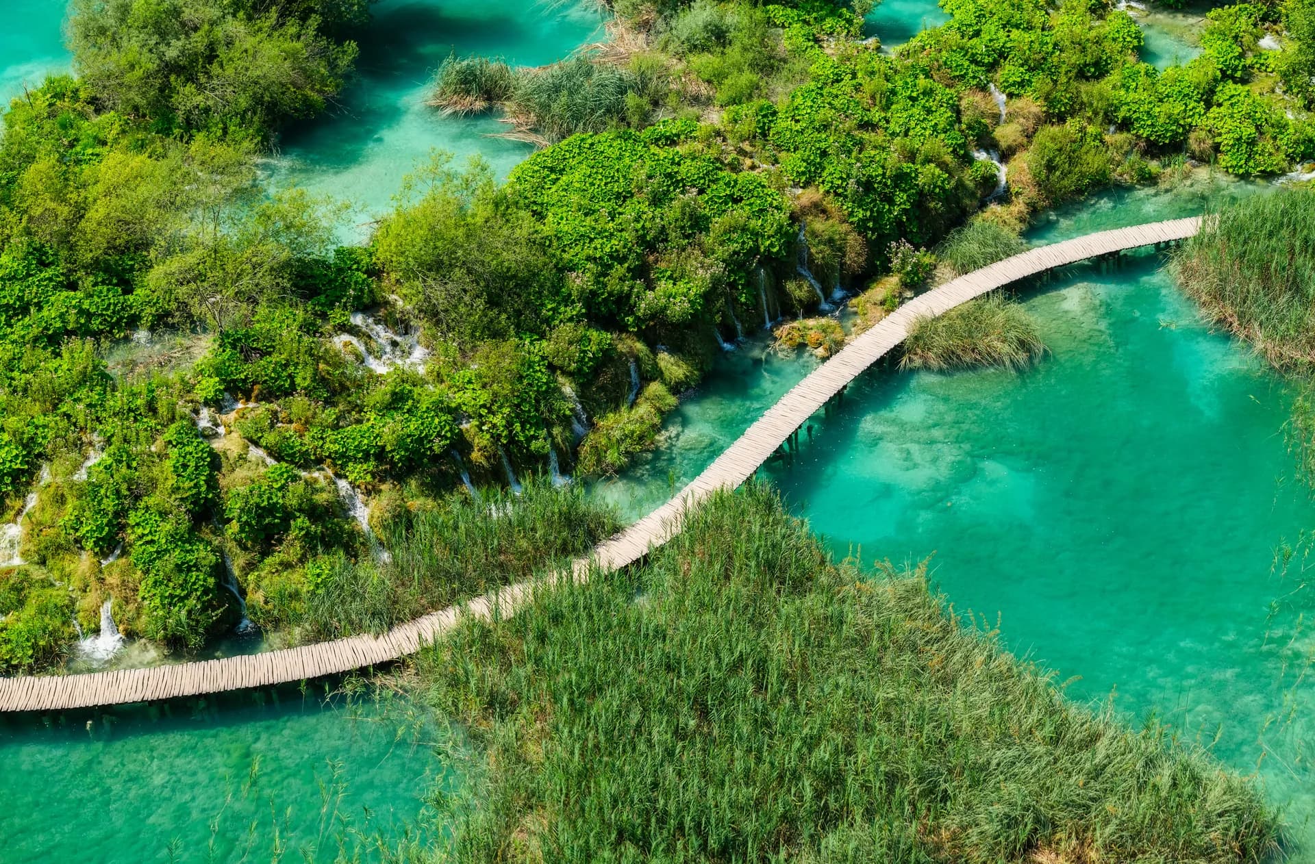 A wooden boardwalk curves between wooded islands and clear lake water.