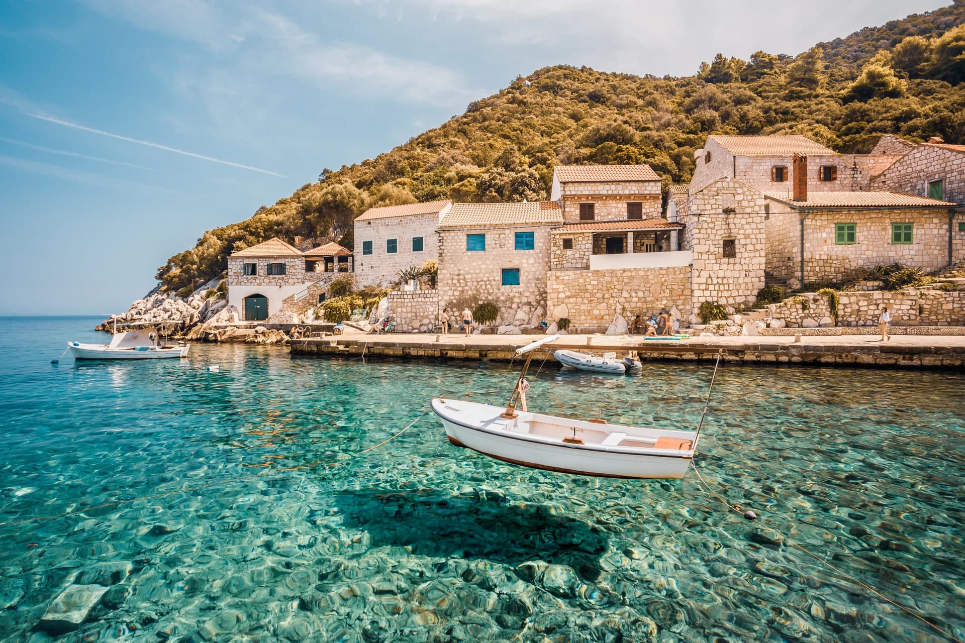 A wooden boat floats in clear water beside stone waterfront houses on Lastovo.