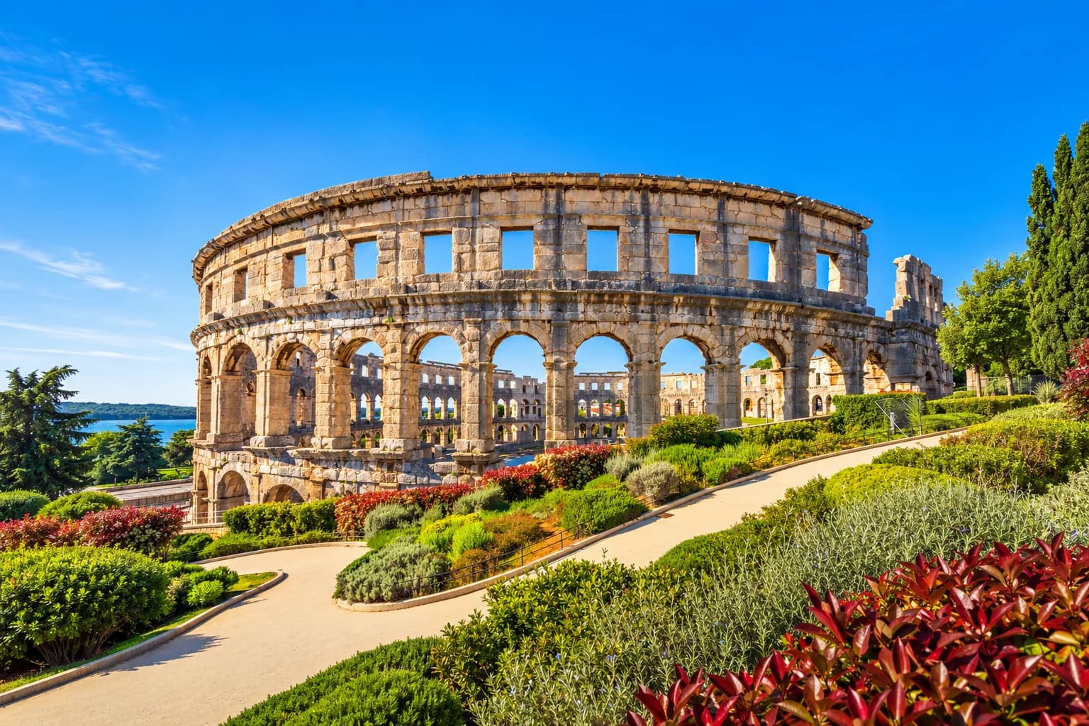 The Roman amphitheatre in Pula, with stone arches above a green garden.