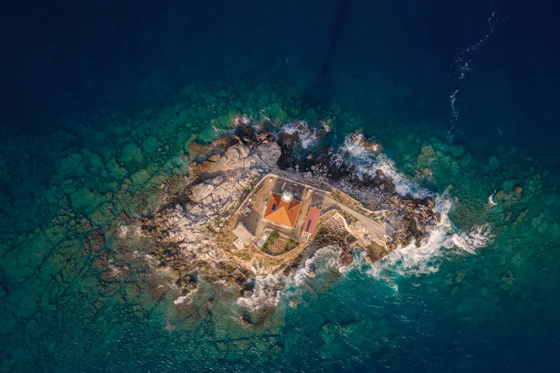 A small lighthouse surrounded by rock and open water.
