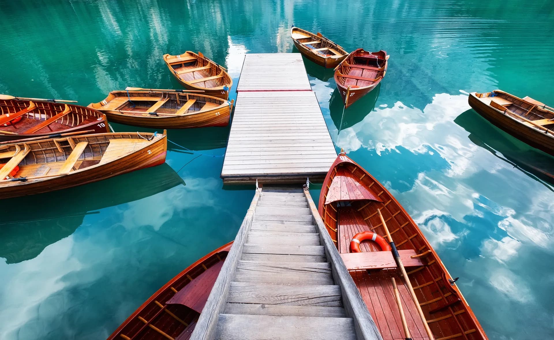 A wooden jetty leads between rowing boats onto a calm mountain lake.