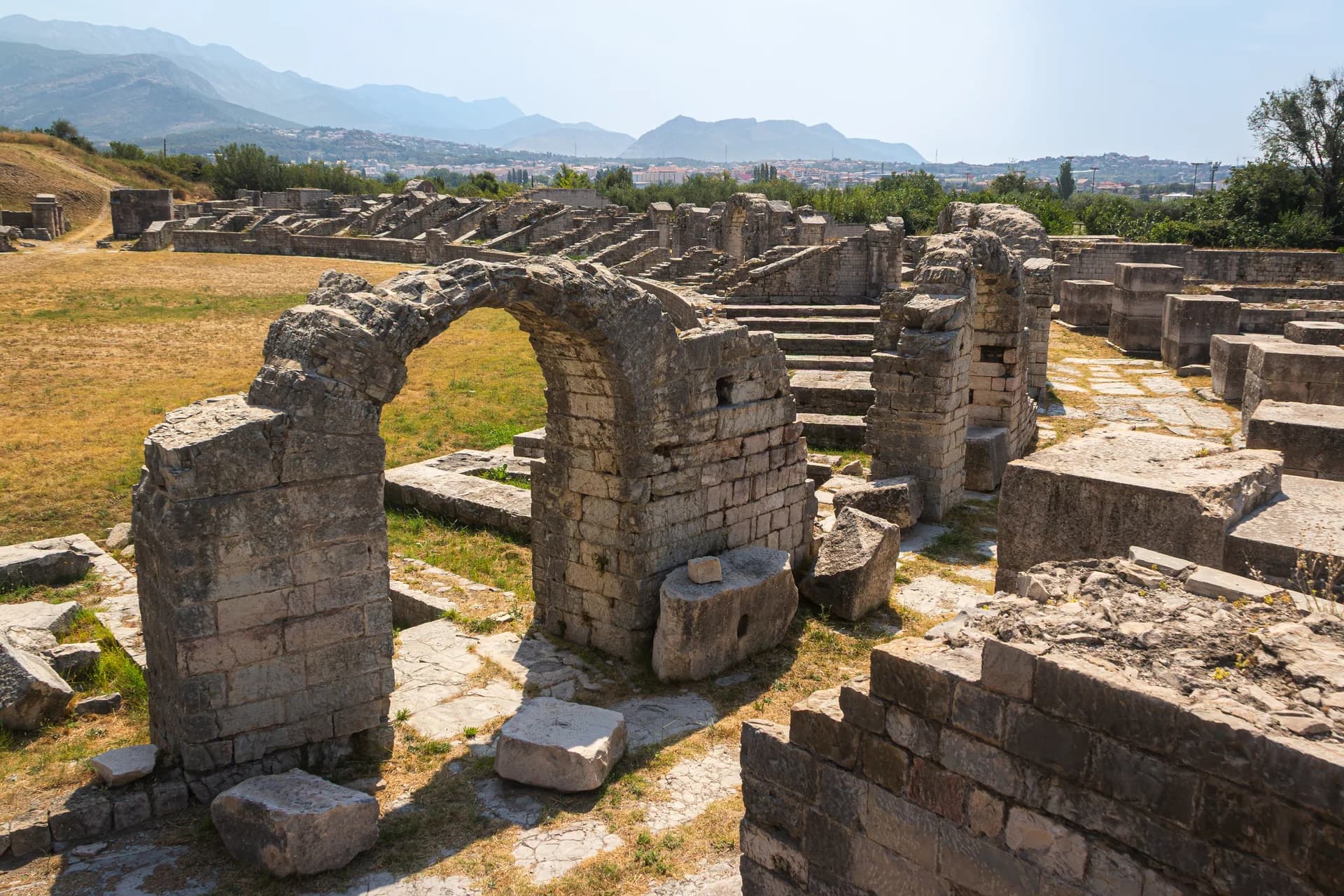 Stone arches and ancient ruins with mountains in the distance.