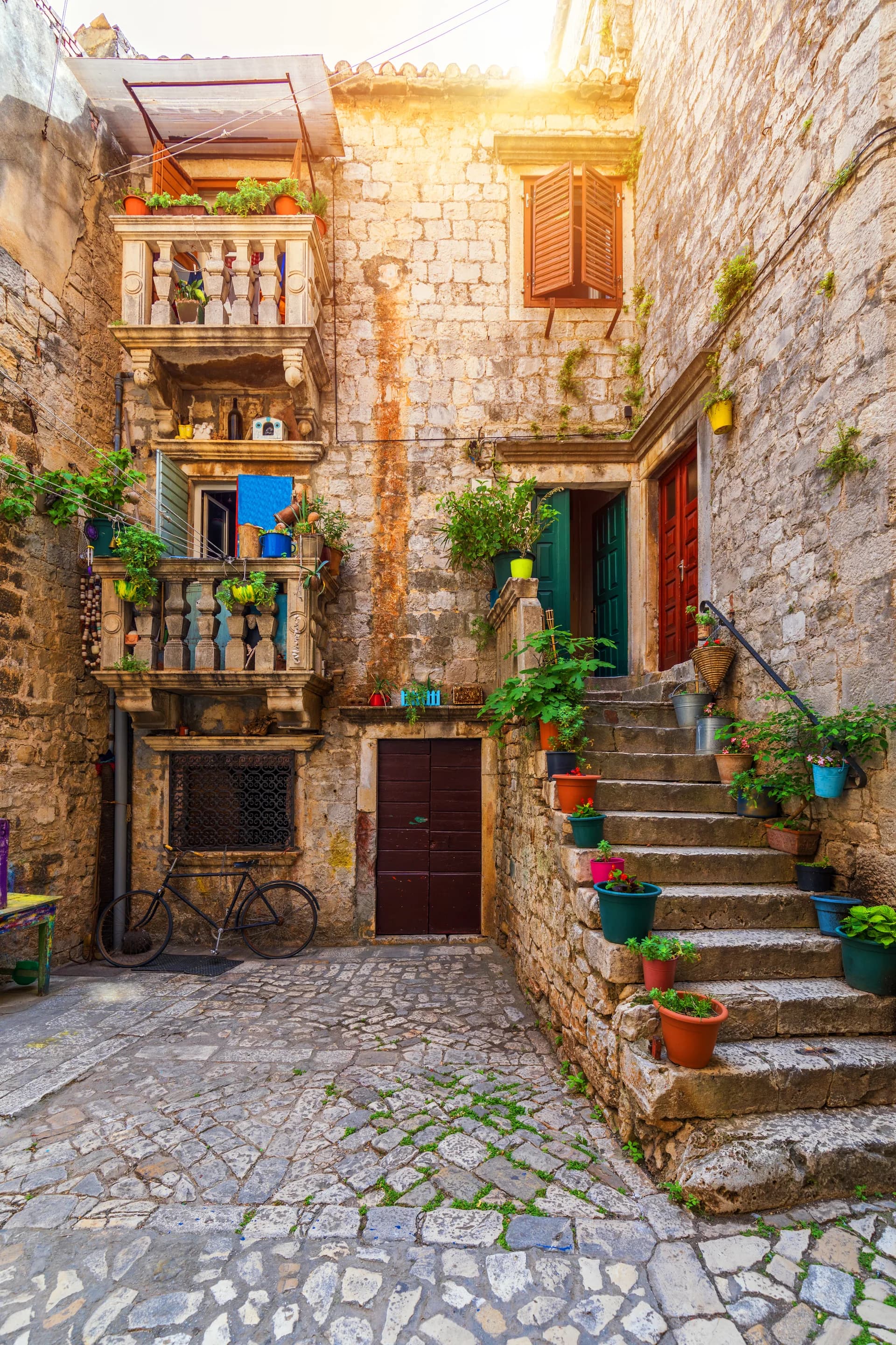 A narrow stone lane framed by balconies, shutters, and climbing plants.