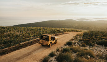 Yellow jeep driving through vineyards on the scenic island of Šolta, with a view of islands and the sea.